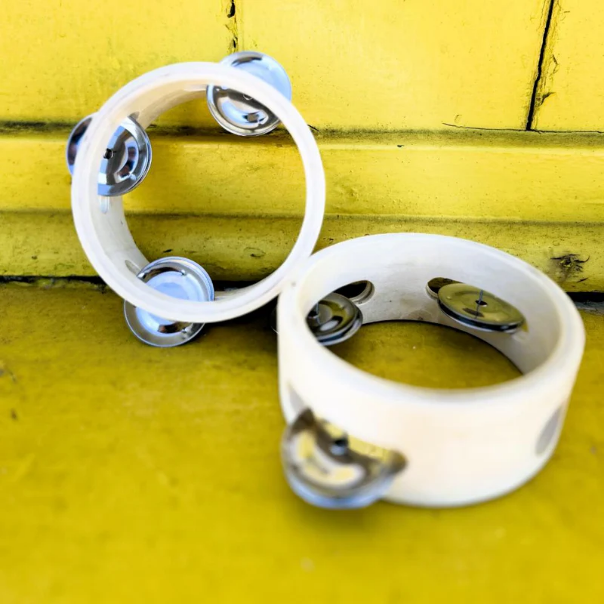 Showing two Make Me Iconic wooden tambourine - durable natural wood tambourine with bright details, perfectly sized for toddlers to explore sound, rhythm, and creativity through hands-on musical play.