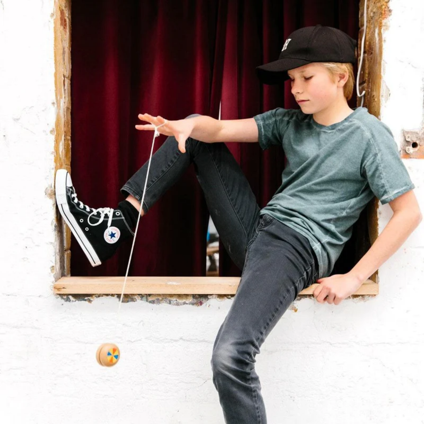 Played by a boy sitting on a window Make Me Iconic wooden yo-yo toy - durable timber yo-yo with retro-style painted designs, crafted for smooth spinning and easy tricks, a nostalgic skill toy for kids and adults.