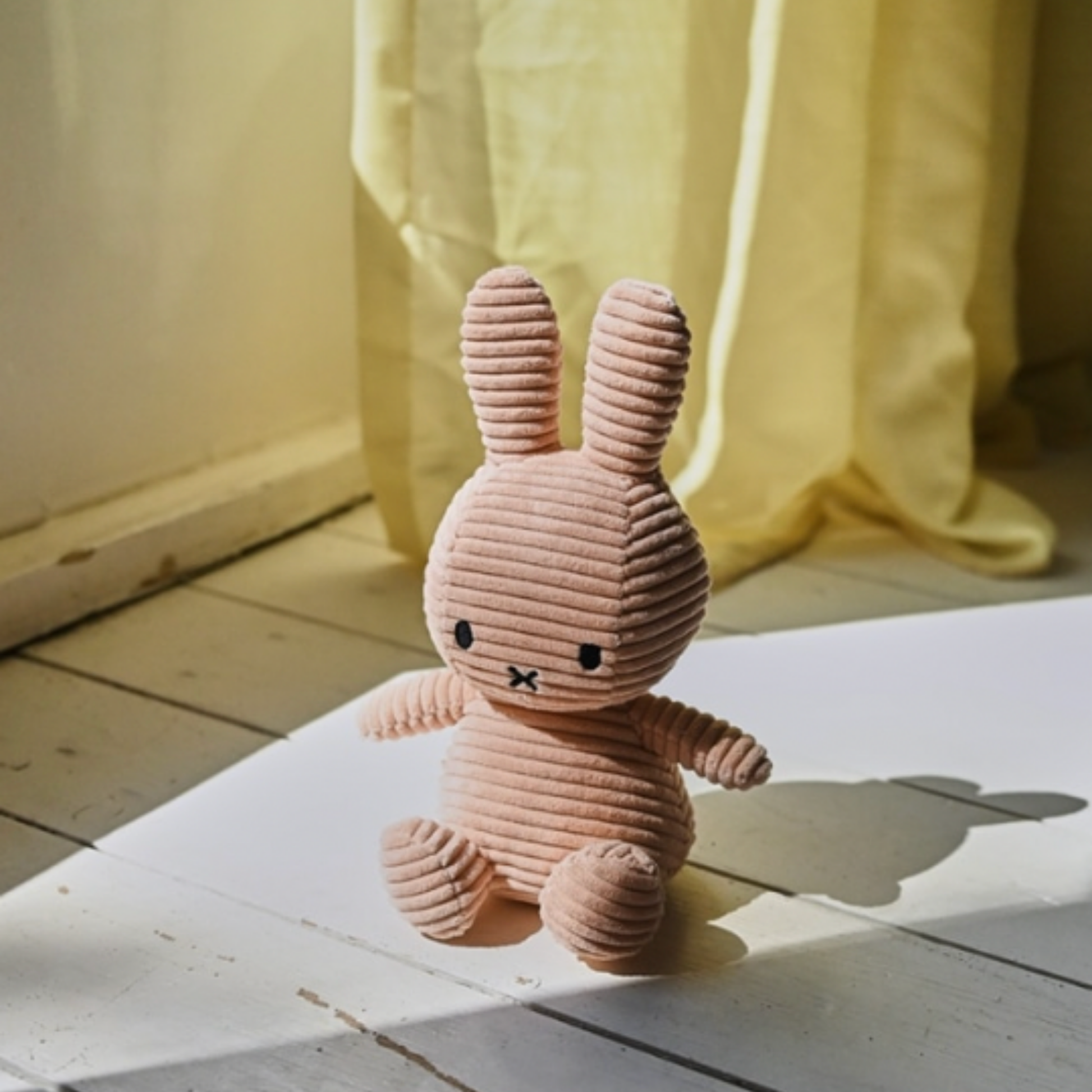 Sitting Miffy 23cm beige displayed on white floor boards infront of yellow curtain
