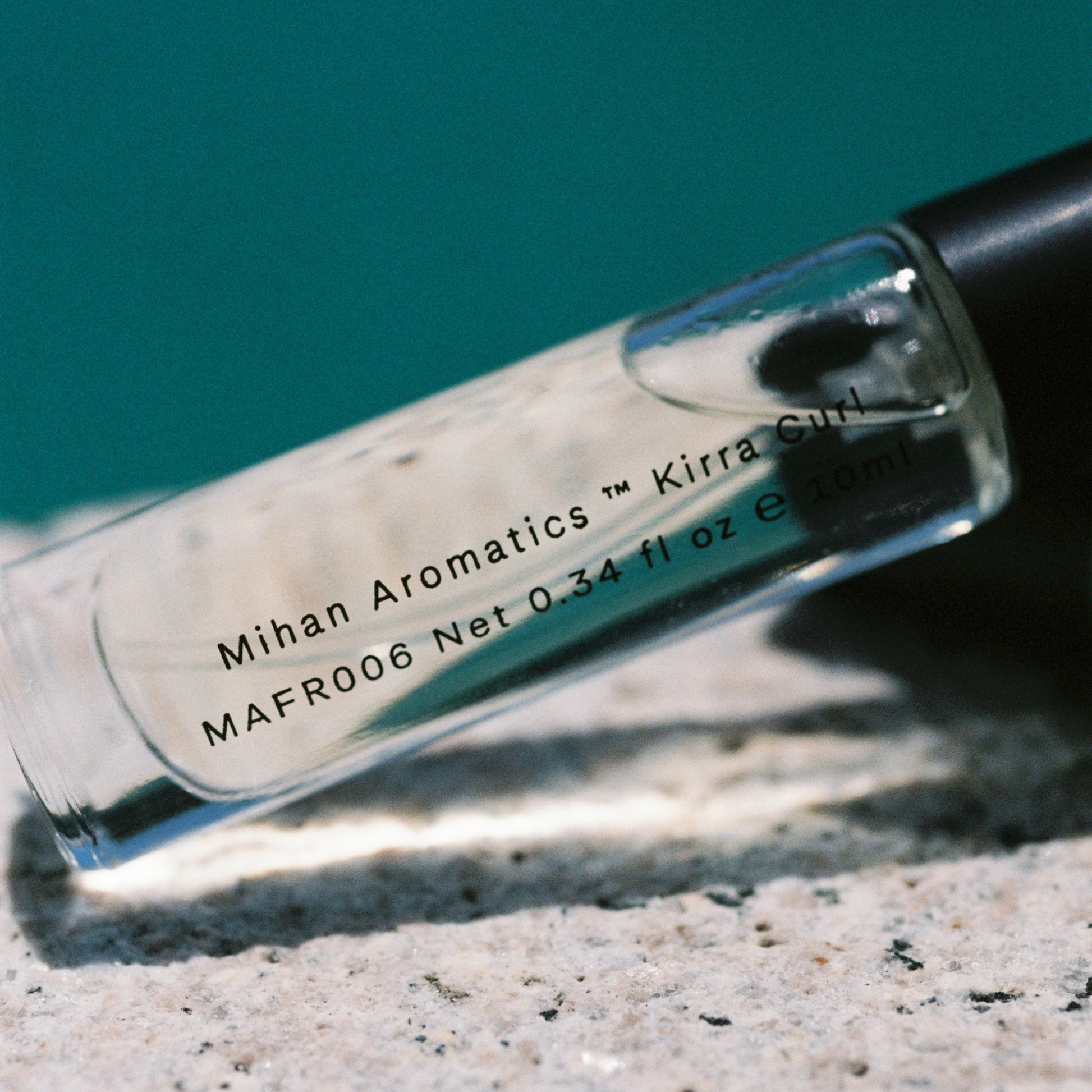 Upclose view of Mihan Aromatics Kirra Curl Parfum in clear glass bottle, 10ml, woody amber scent blending sea salt, lemon rind, leather, surf wax, and Australian sandalwood. Inspired by sun-soaked surf days along the Australian coast. Hand-filled in Melbourne, cruelty-free and vegan, with 30% perfume concentrate for lasting fragrance.