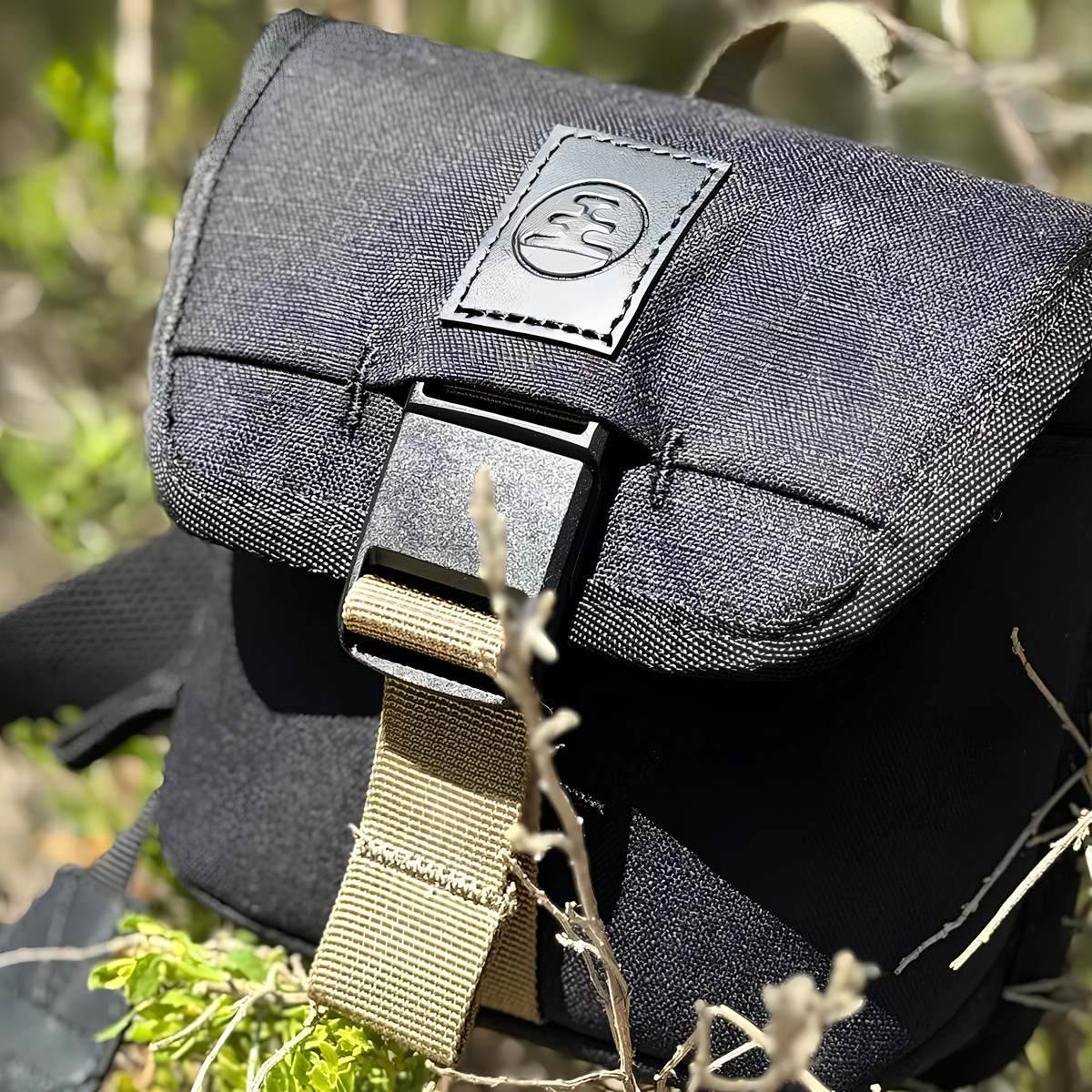 Nocs Provisions Binocular Standard Issue Pouch in charcoal black, recycled abrasion-resistant fabric with secure NocLoc closure, universal strap attachments and internal storage pocket, for a 25mm binocular, shown sitting on the grass.