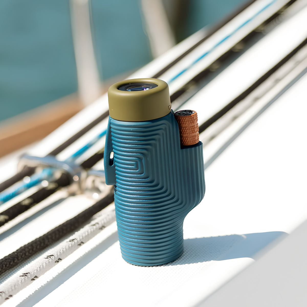 Nocs Provisions Monocular Zoom Tube 8X32 Indigo Blue that has fully multi-coated optics, premium BaK4, high quality optical glass, water resistant and compact, shown standing on a boat edge.