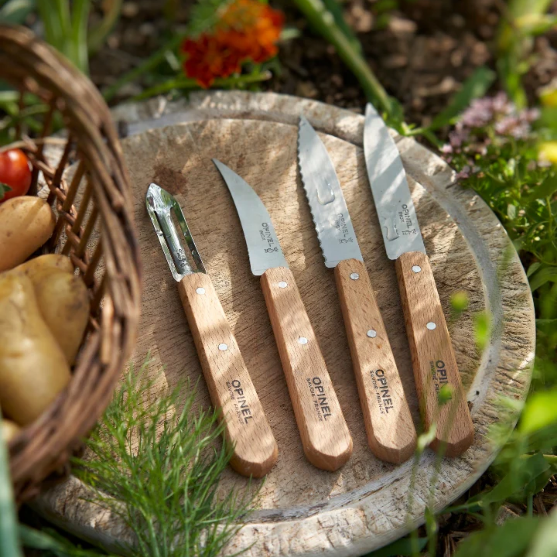 On a circle wood the four knives from Opinel Les Essentiels Kitchen Utility 4PC Set - Stainless steel kitchen knife set with hornbeam wood handles - Includes paring knife, serrated paring knife, vegetable knife, and peeler for versatile meal prep - Durable French-made cutlery set ideal for slicing, peeling, and garnishing fruits and vegetables - Essential kitchen tool set combining quality craftsmanship and everyday use