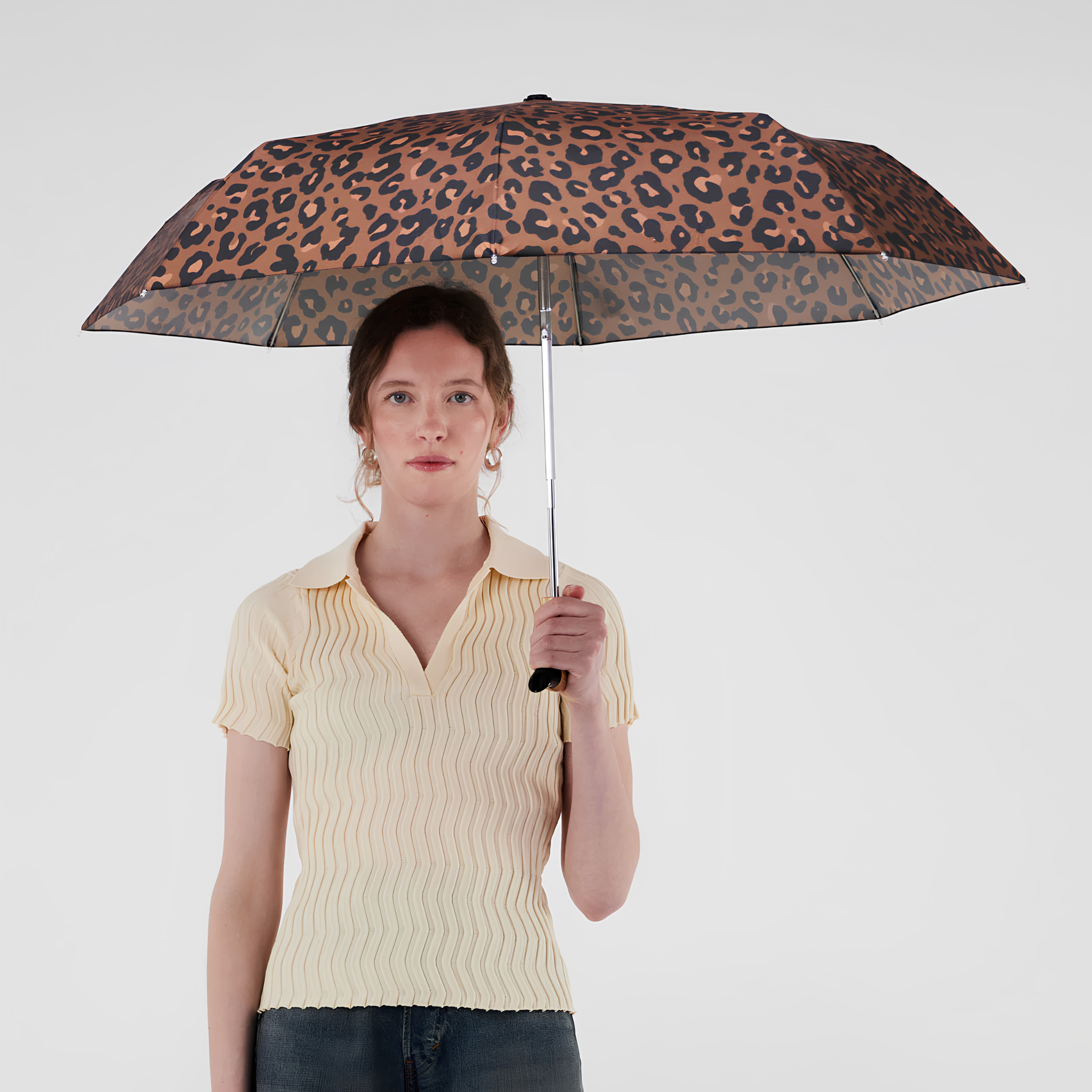 A woman holding the open Original Duckhead Duck Umbrella Compact Leopard timeless animal print design from sustainable materials.