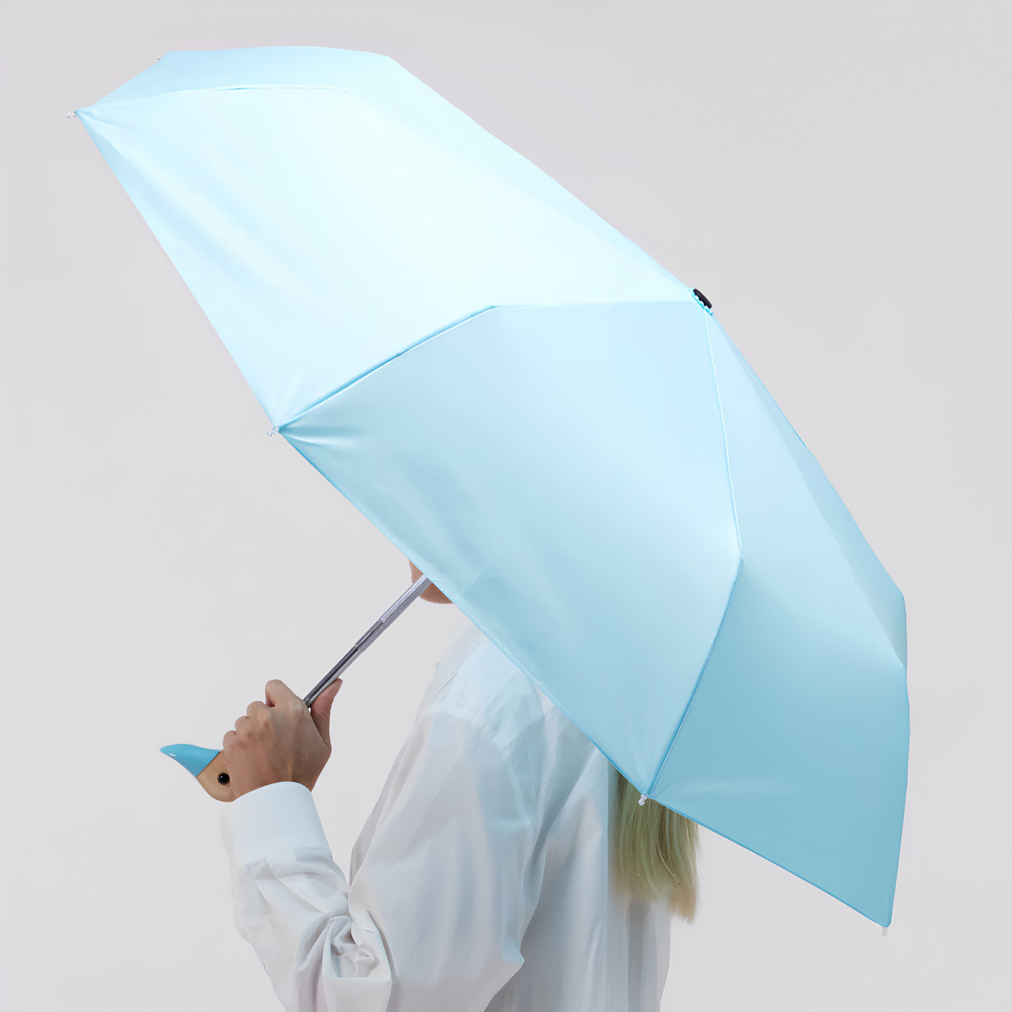 A woman holding the open side view Original Duckhead Duck Umbrella Compact Popsicle Blue or sky inspired, from sustainable materials.