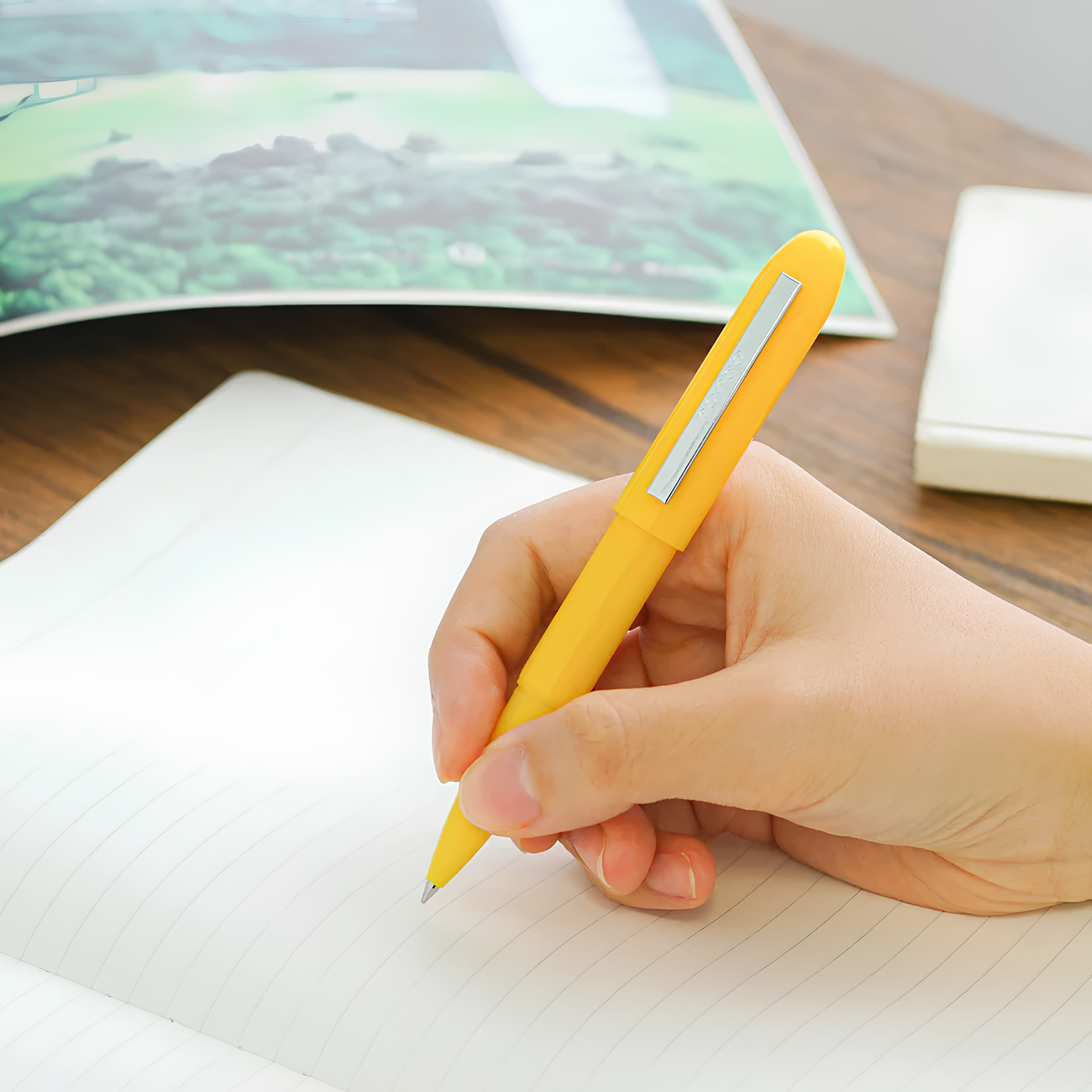 Shown held by a hand in writing, the Penco Bullet Ballpoint Pen Yellow Pen light, 93mm long with black ink, easy to slip in your pocket or purse.