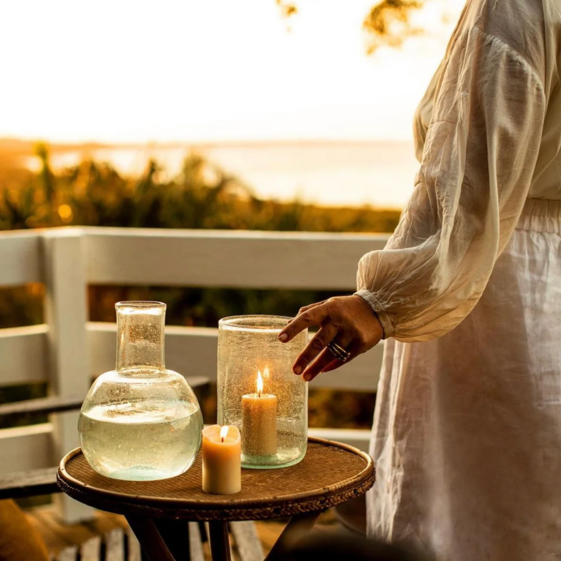 Queen Bee beeswax pillar candle 8cm lit on balcony while sun setting with woman in background