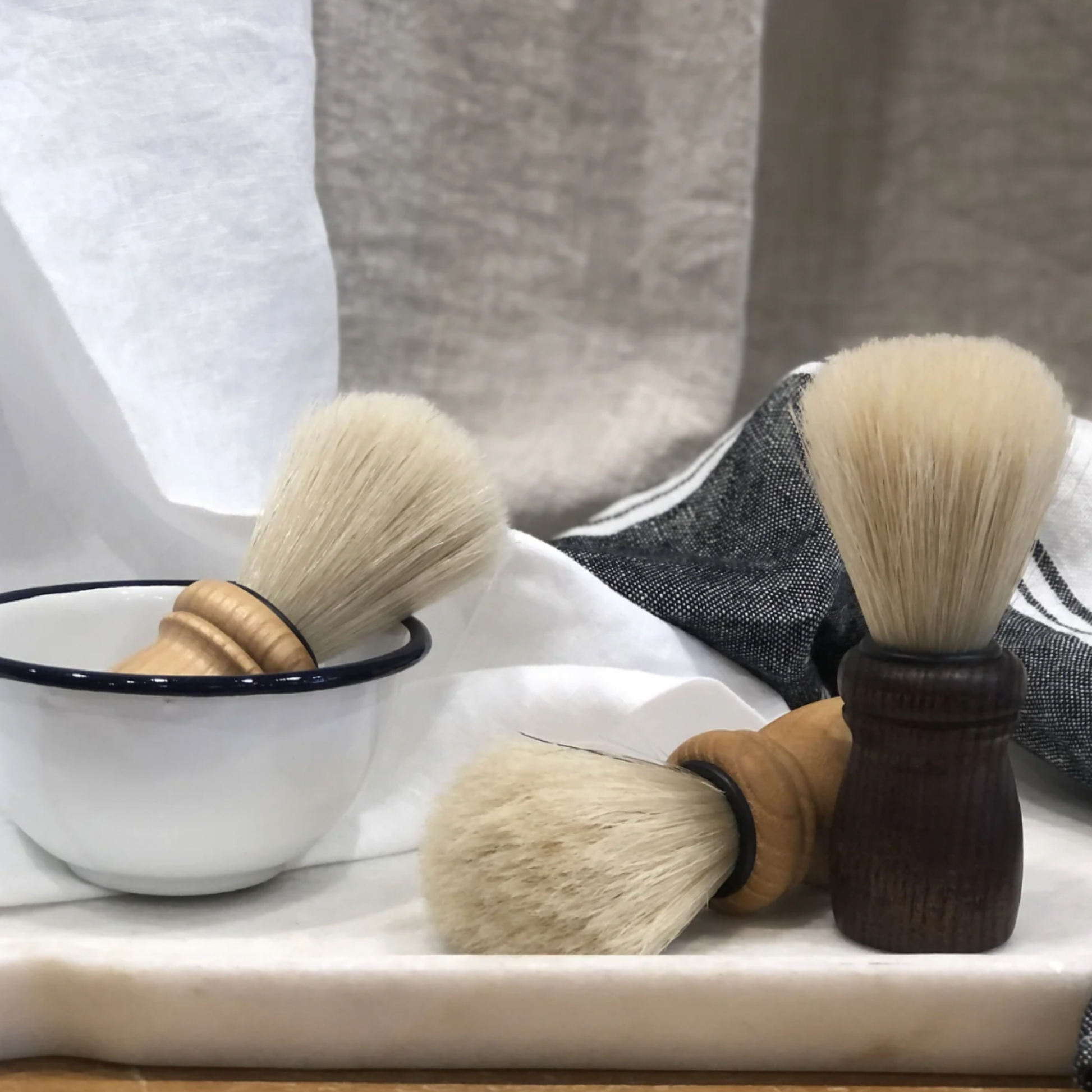 Assorted Redecker shaving brushed on display infront of linen in a bowl 