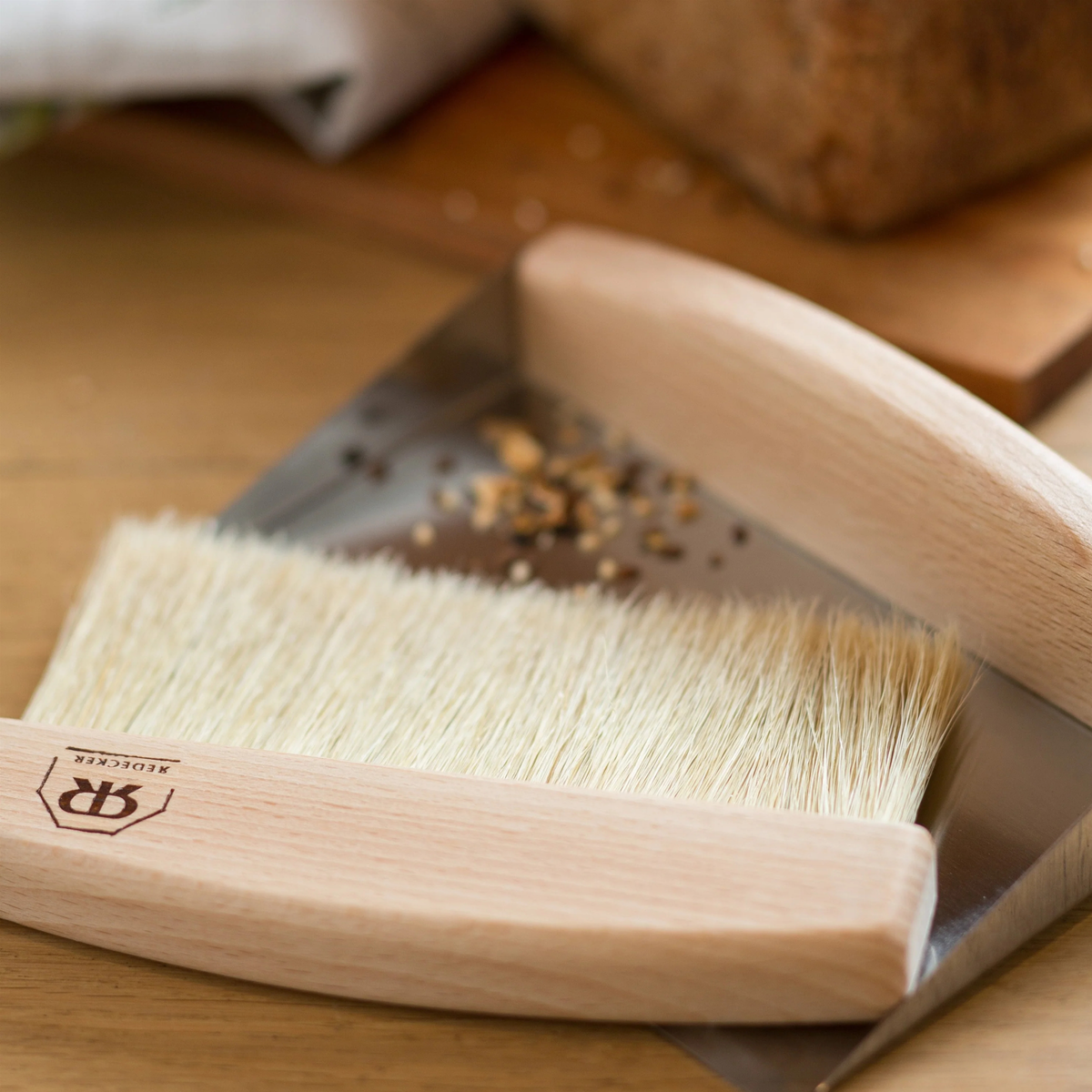 Redecker Table Sweeping Set light brown on the floor, made from stainless steel and soft natural bristles which includes a sleek tray and matching hand brush detachable by a magnet.