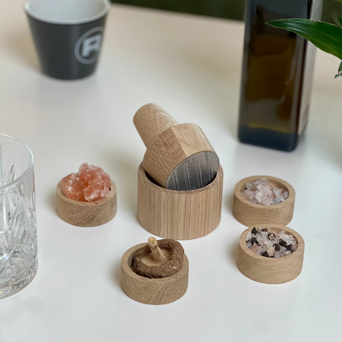 Showing different spices and salt and the Rivsalt salt and spice mortar crush in oak wood with stainless steel blades, a compact manual grinder designed for crushing rock salt and dried spices. Includes a small cleaning brush and comes in a Swedish-designed cardboard gift box.