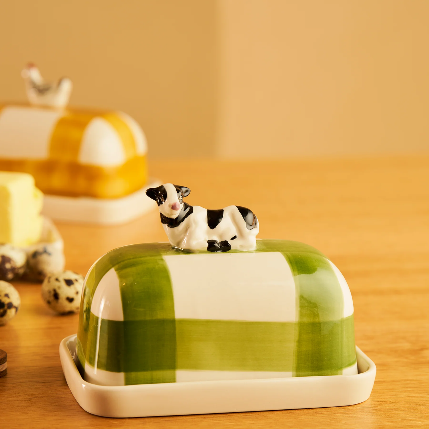 Side view of the Robert Gordon Butter Dish Cow made from high fired porcelain with green brushwork lines and a hand-painted cow perched on top.