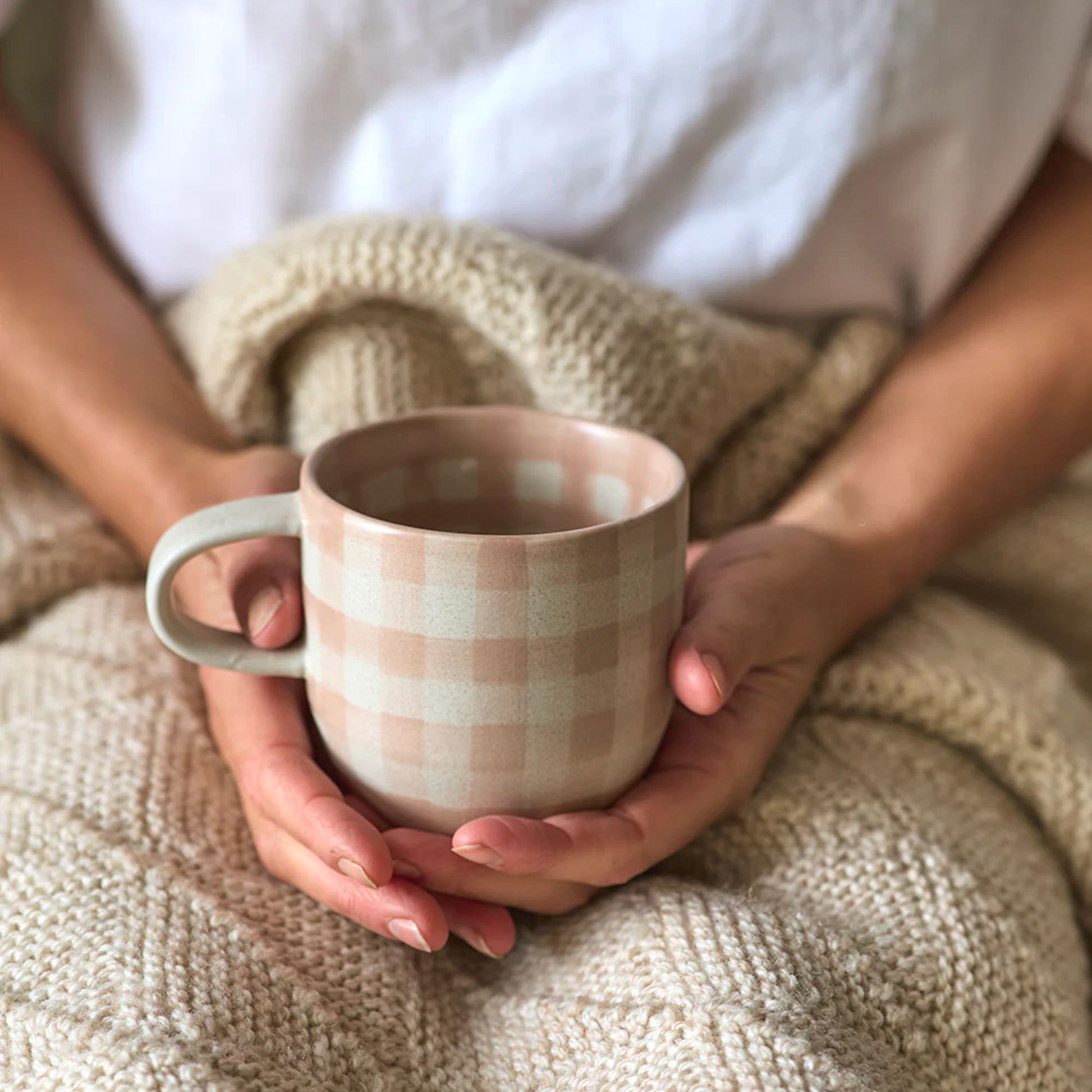 Woman holding Robert Gordon cats pyjamas mug soft terracotta check in hands wrapped in blanket