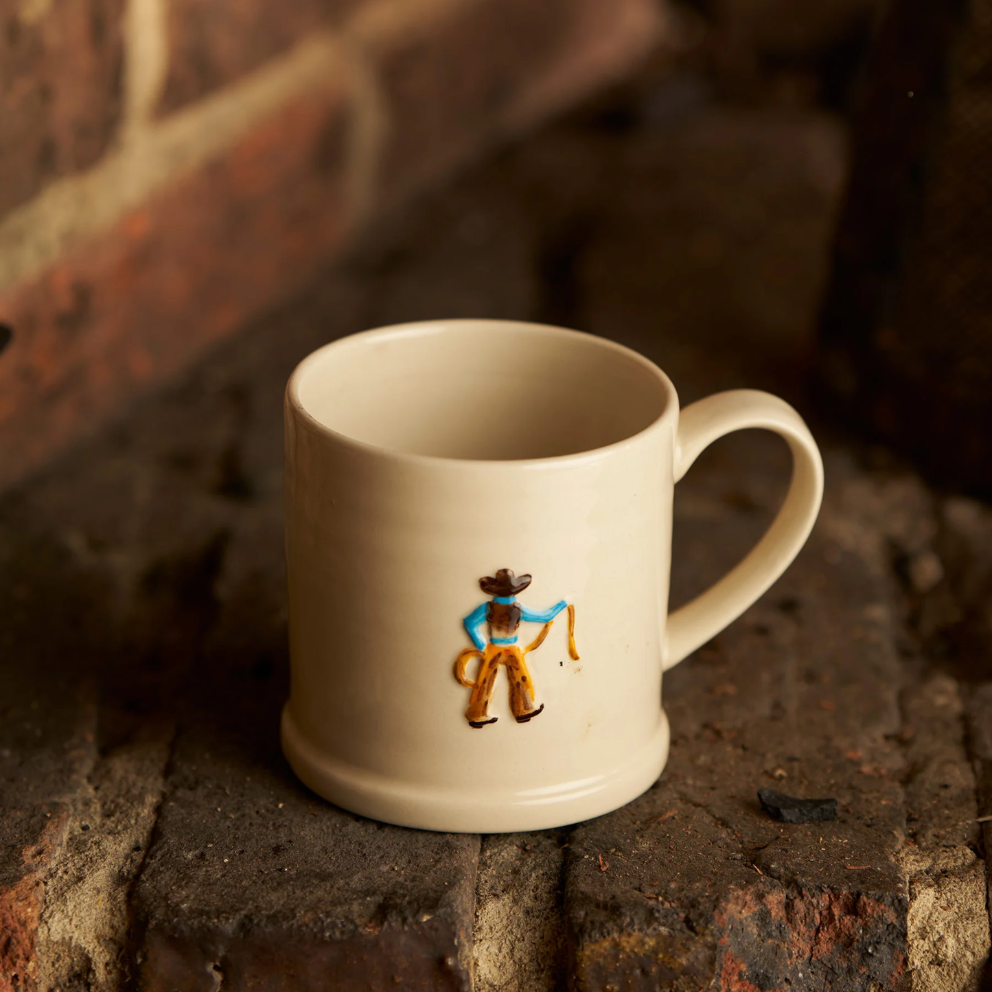 Front view of the Robert Gordon Favourite Things Mug Large on a brick, made from stoneware with Cowboy motif painted by hand with 310ml capacity.
