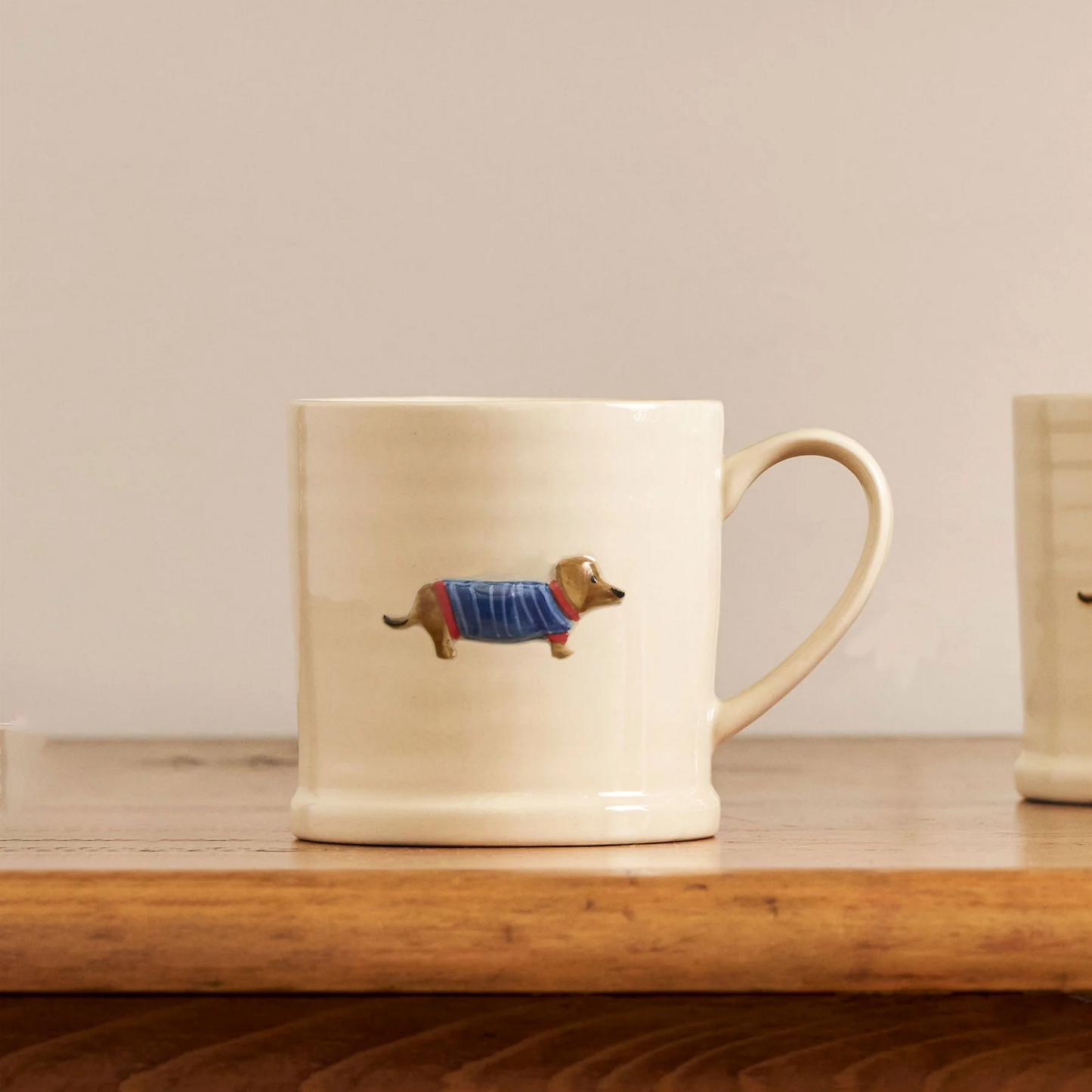 On a wooden table, the Robert Gordon Favourite Things Mug Large with a quirky hand painted character design Dachshund.