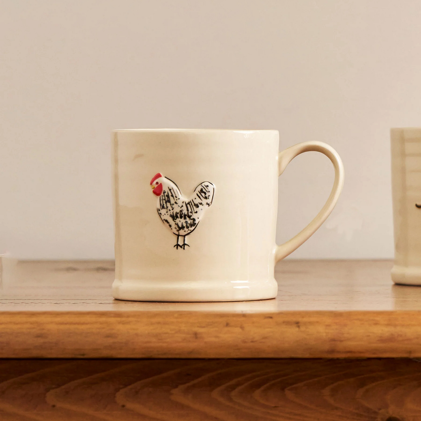 On a wooden table, the Robert Gordon Favourite Things Mug Large with a quirky character Spotted Hen that is hand painted.