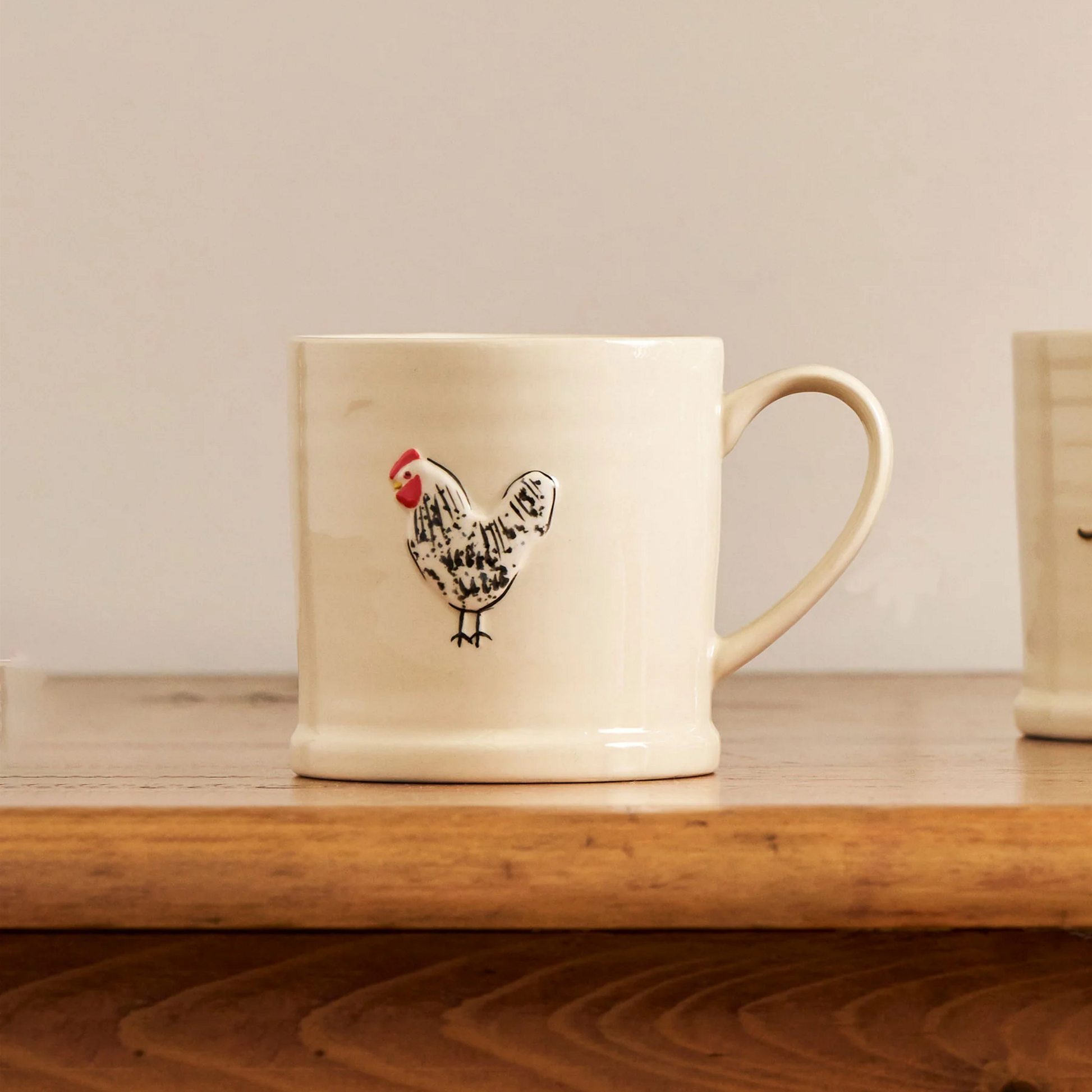 On a wooden table, the Robert Gordon Favourite Things Mug Large with a quirky character Spotted Hen that is hand painted.