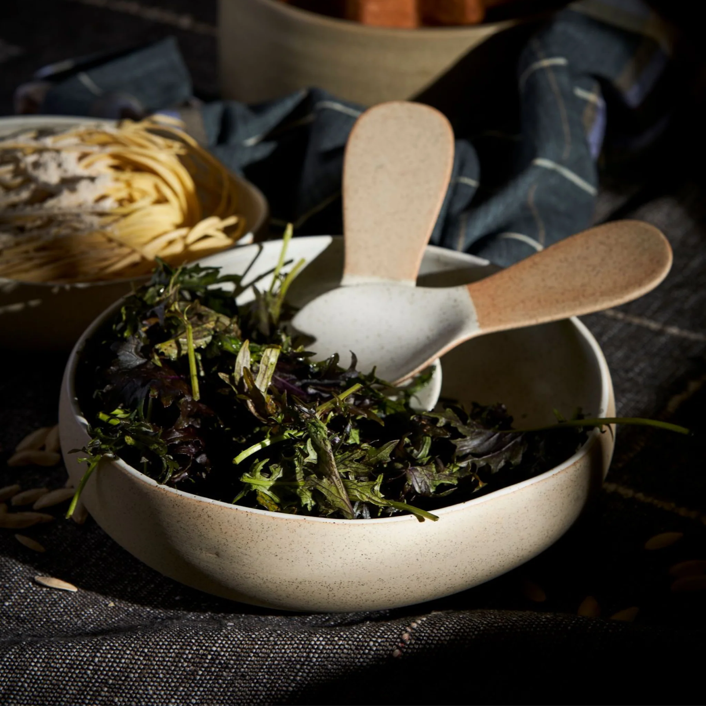 Showing green leaf salad on the Robert Gordon Garden To Table Bowl 26.5cm Beige and white which is an Earthly clay body with light organic glaze, hand crafted made from stoneware, microwave and dishwasher safe, designed in Australia, made in China.