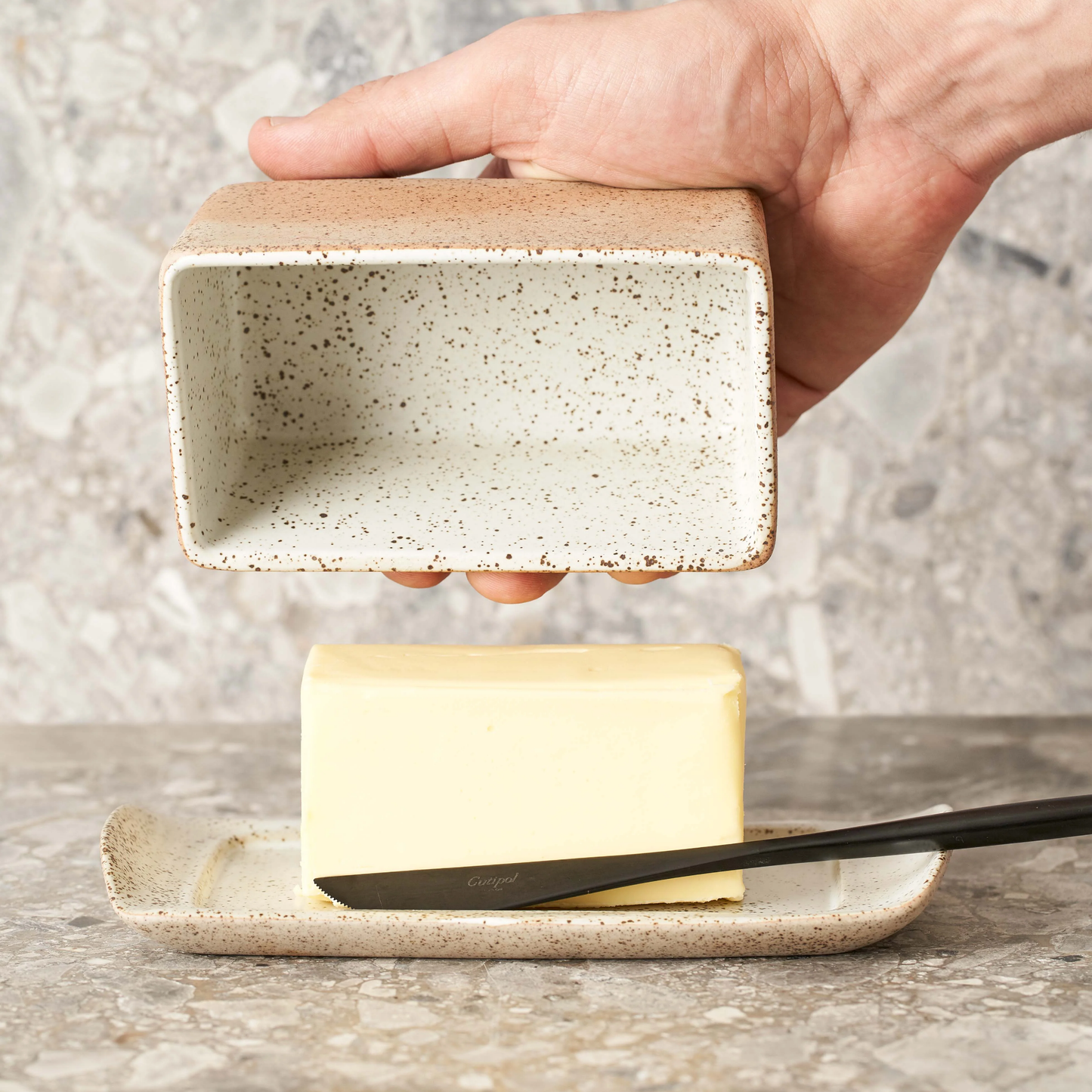 Man opening Robert Gordon butter dish on marble table side view with knife