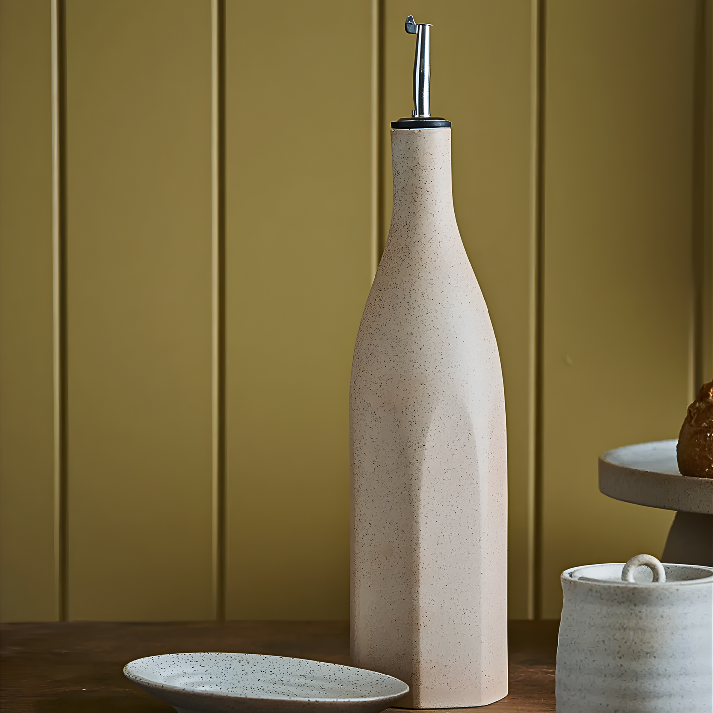 Seen on a wooden table, the Robert Gordon Garden To Table Olive Oil Bottle 750ml Earthly clay body with speckles, light organic glaze, hand crafted made from stoneware, microwave and dishwasher safe, designed in Australia, made in China.
