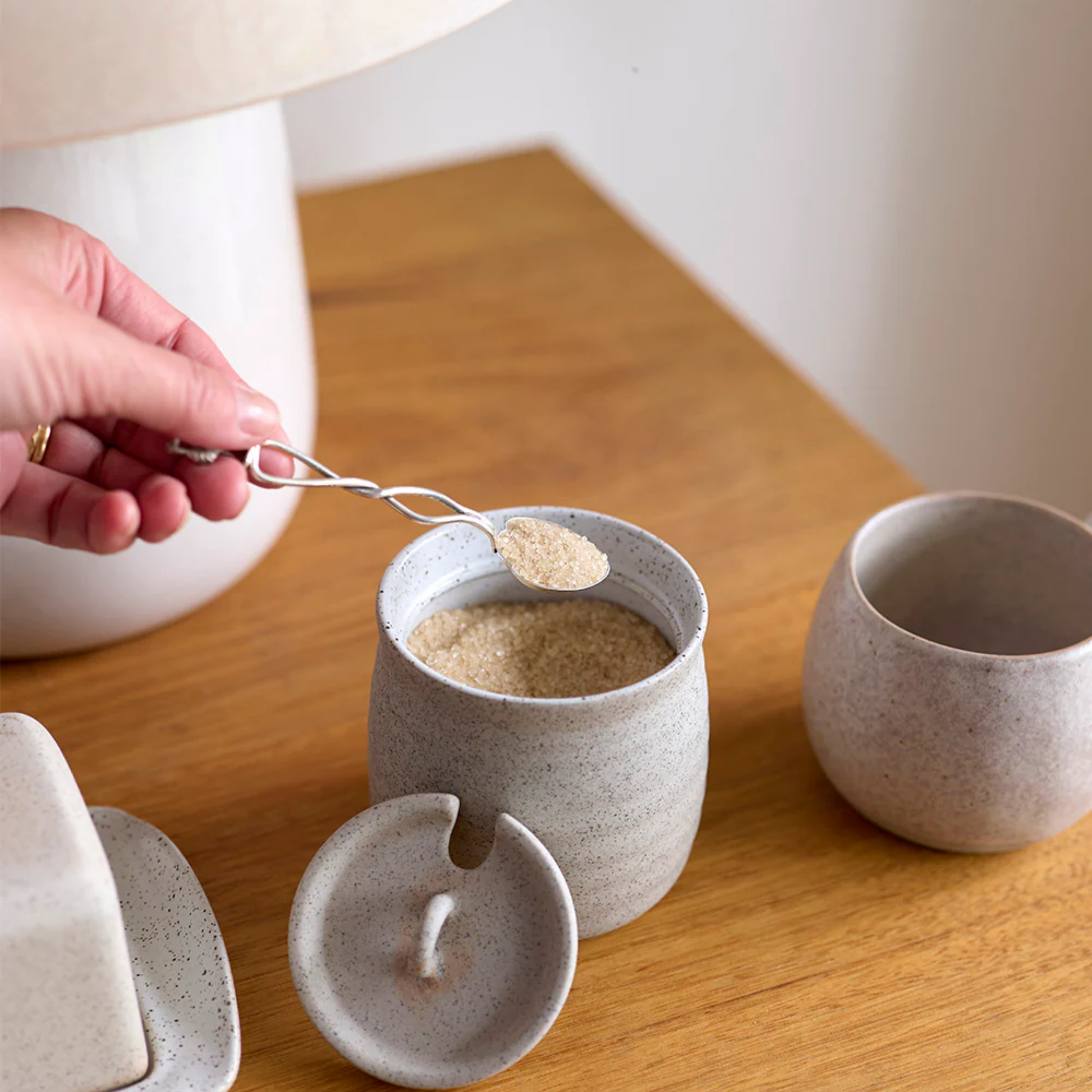 Woman using spoon to scoop out sugar out of sugar bowl on wooden table