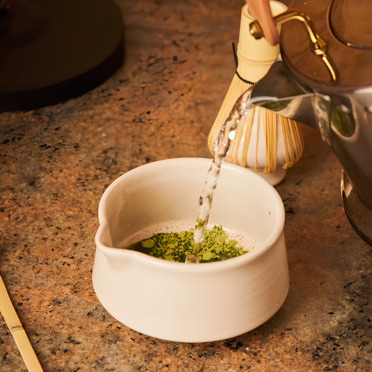 Pouring water in to the bowl from Robert Gordon Matcha 4 Piece Set Milk for traditional ceremonial matcha with a whisk holder and bamboo whisk and scoop beside it.