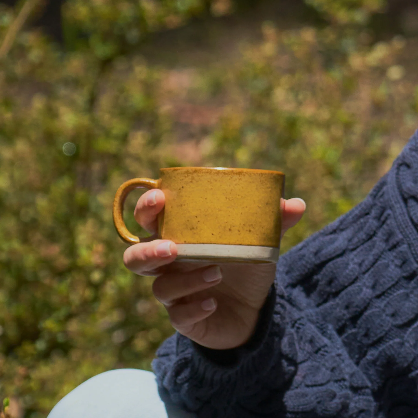 On outdoor a woman holding one of the Robert Gordon Mineral Mugs (set of 4) Citrine 270ml capacity signature artisan craftmanship reactive glaze finish with speckles, made from durable stoneware, microwave and dishwasher safe, designed in Australia, made in China.