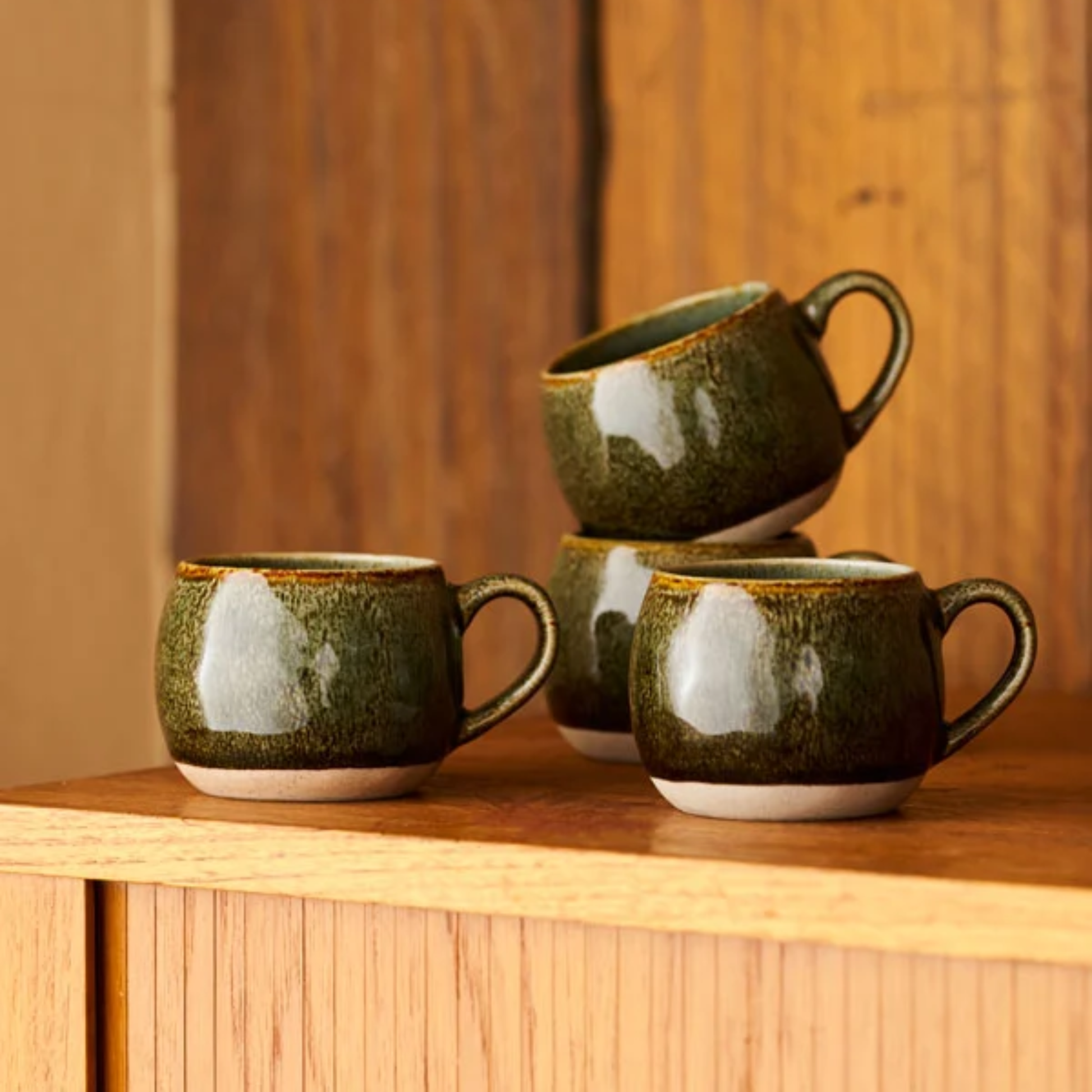 Robert Gordon Mineral Mugs (set of 4) Serpentine on top of a wooden surface, featuring its reactive glaze finish over an earthly clay body durable stoneware.