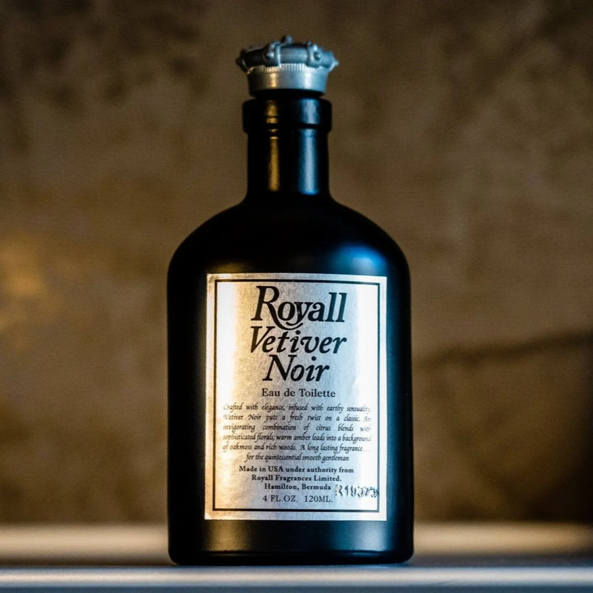 Close up on the Royall Lyme Bermuda Vetiver Noir, black hand-made glass bottle with pewter-colored crown cap and white label, displayed on a plain white background.