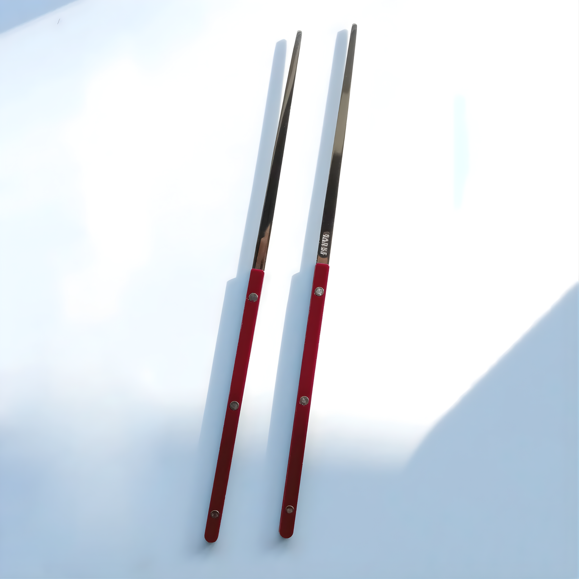 On a surface, the Sabre Bistrot Cutlery Chopsticks 23cm (pair) Burgundy, which is made from Inox 18/10 - Manche nylon, not dishwasher safe and not suitable in microwave oven, ergonomic design for comfortable grip, ideal for enjoying dishes such as sushi or noodles.
