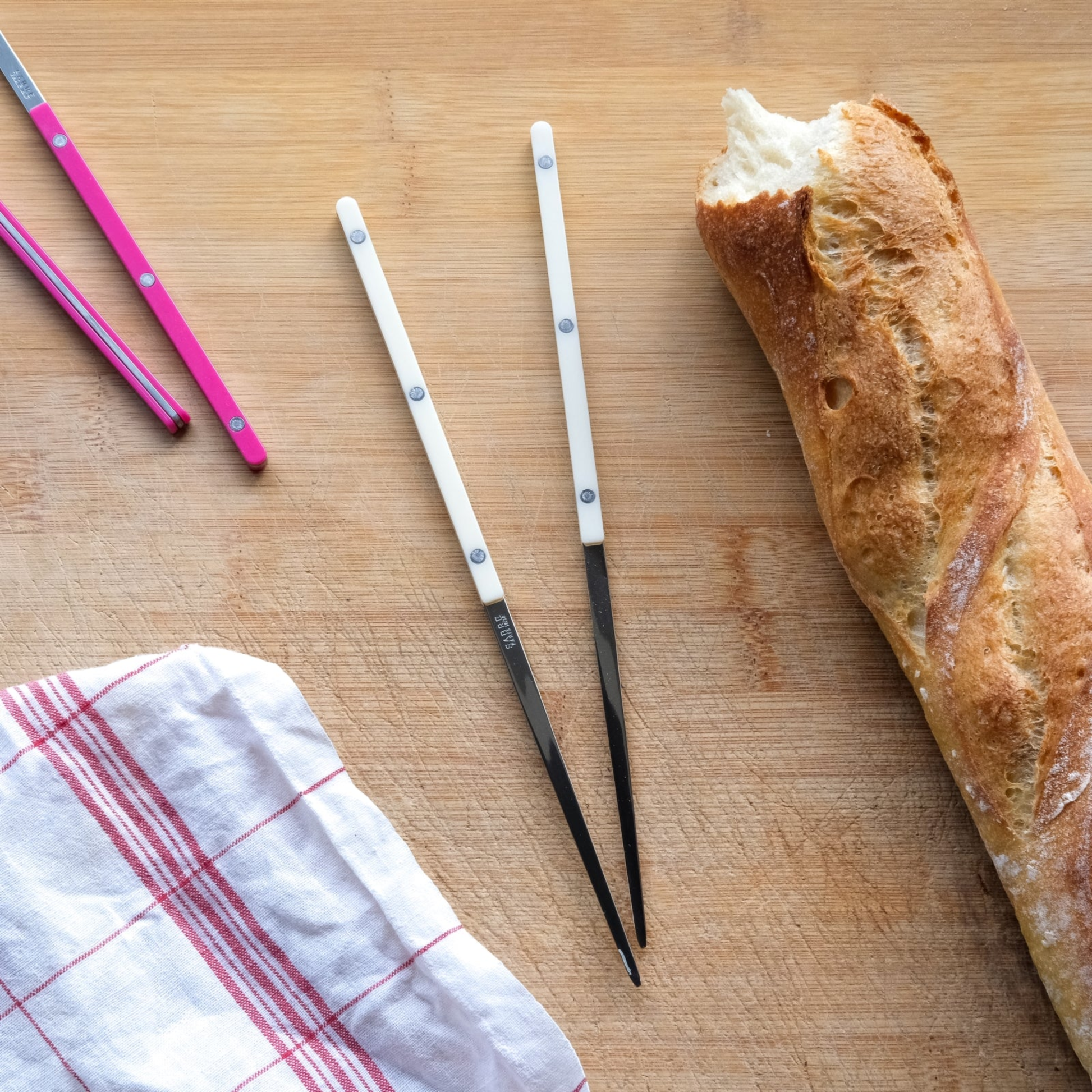 Seen with a bread on a surface the Sabre Bistrot Cutlery Chopsticks 23cm (pair) Ivory, which is made from Inox 18/10 - Manche nylon, not dishwasher safe and not suitable in microwave oven, ergonomic design for comfortable grip, ideal for enjoying dishes such as sushi or noodles.