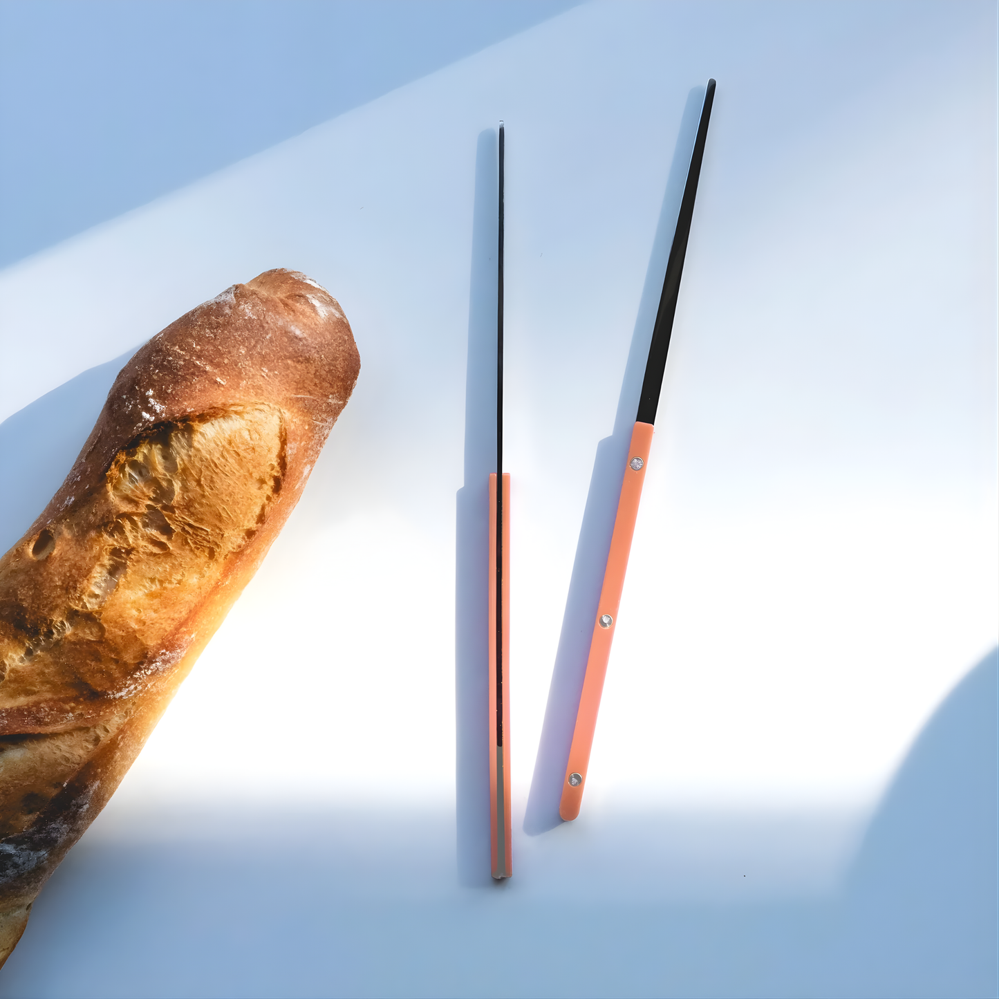 Seen with a bread on a surface the Sabre Bistrot Cutlery Chopsticks 23cm (pair) Nude pink, which is made from Inox 18/10 - Manche nylon, not dishwasher safe and not suitable in microwave oven, ergonomic design for comfortable grip, ideal for enjoying dishes such as sushi or noodles.