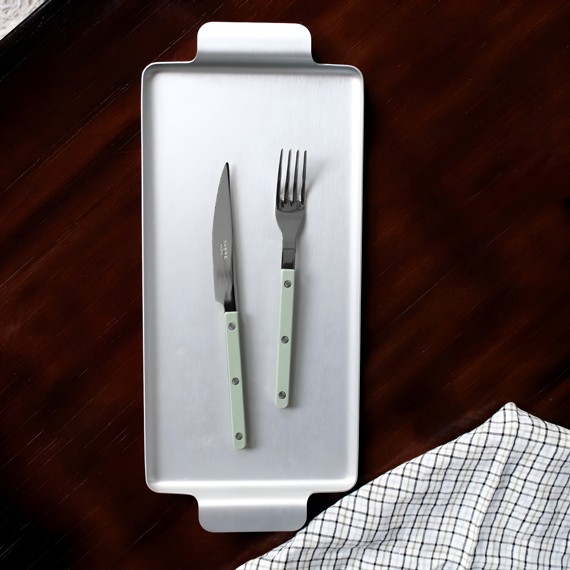 On a silver tray with a knife, the Sabre Bistrot Cutlery Fork 22cm Asparagus, which is made from stainless steel and Inox 18/10 - Manche nylon, dishwasher safe at 113°F (45°C) maximum. Vital part of your dinner set at every stage of the meal.