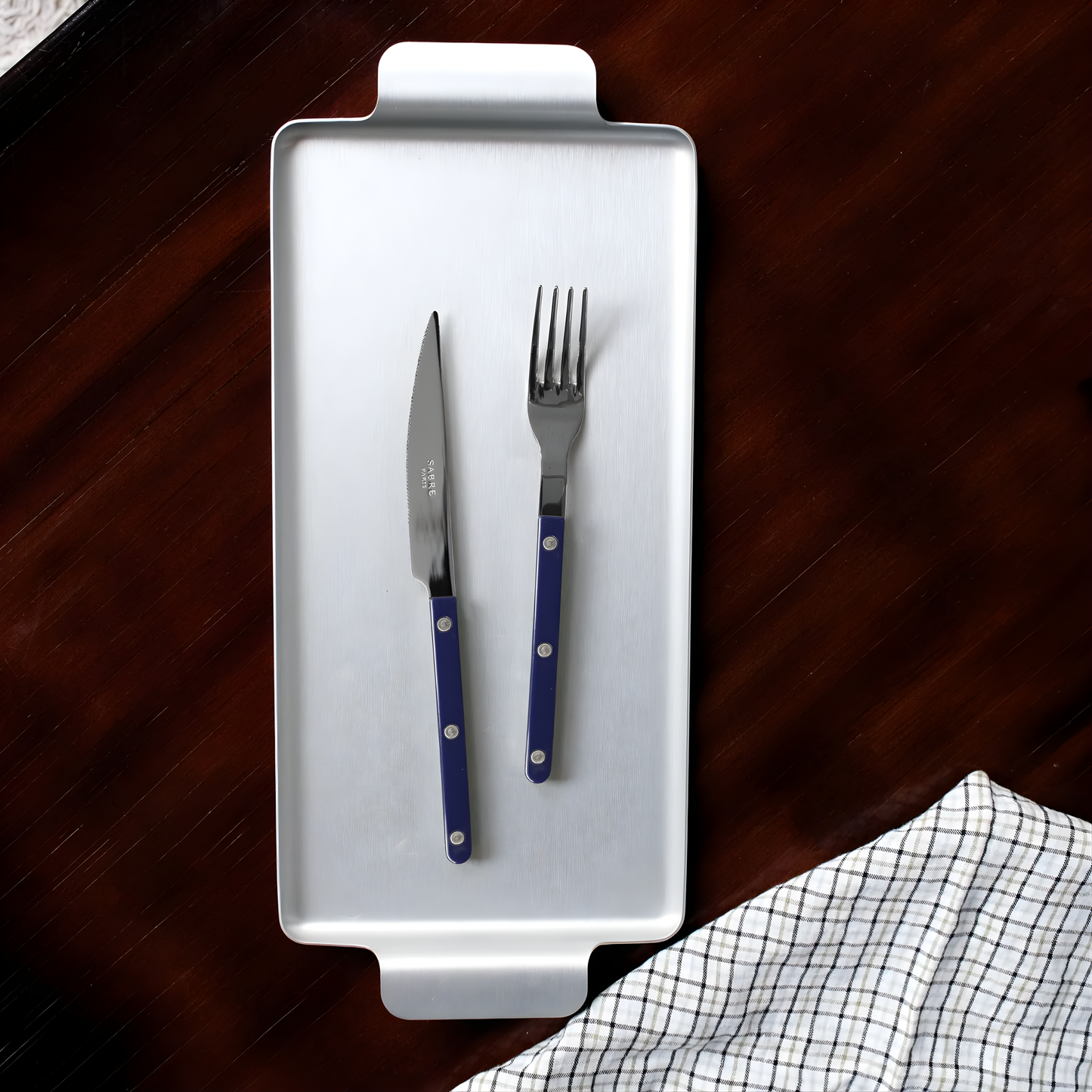 Shown on a silver tray with a knife, the Sabre Bistrot Cutlery Fork 22cm Navy Blue which is made from Inox 18/10 Manche, stainless steel designed to be both traditional and contemporary, dishwasher safe at 113°F (45°C) maximum, not suitable for microwave oven.