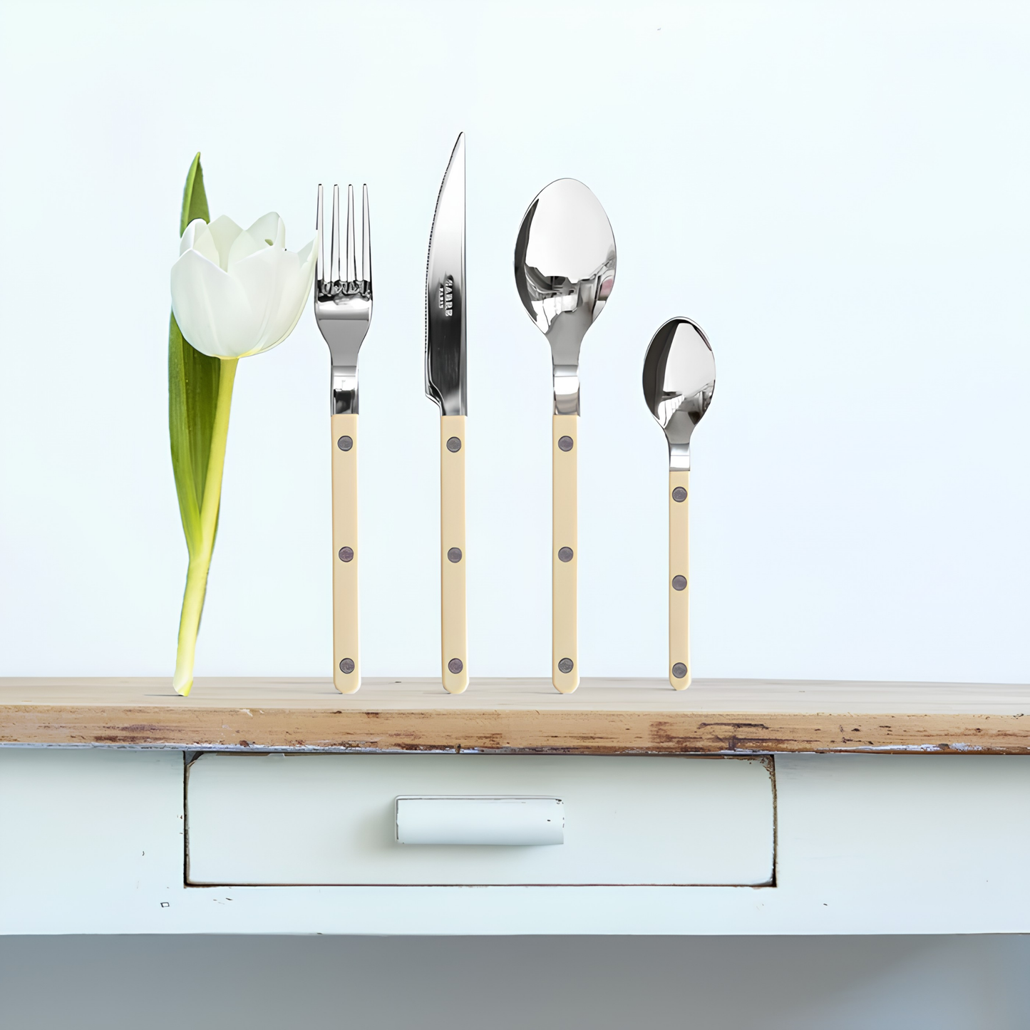 Standing on a wooden cabinet the fork, knife, spoon and teaspoon from Sabre Bistrot Cutlery Ivory 24 Piece Set