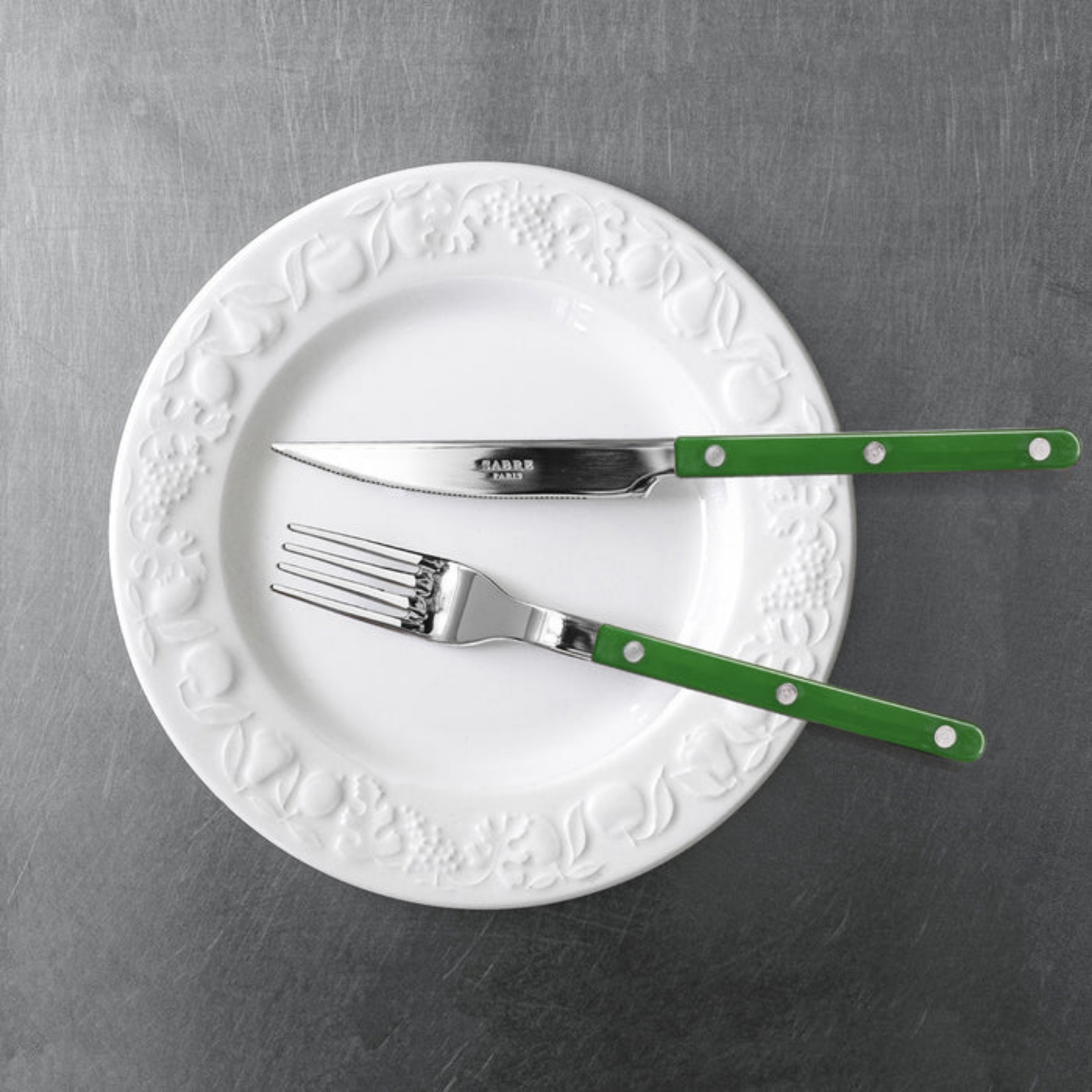 On a plate with a knife Sabre Paris Bistrot Dinner Fork Dark green- 22cm stainless steel fork with colorful nylon handle and visible rivets. Designed in French café style, this durable and elegant fork adds a lively touch to any table setting, available in gloss or vintage finishes and dishwasher-safe.