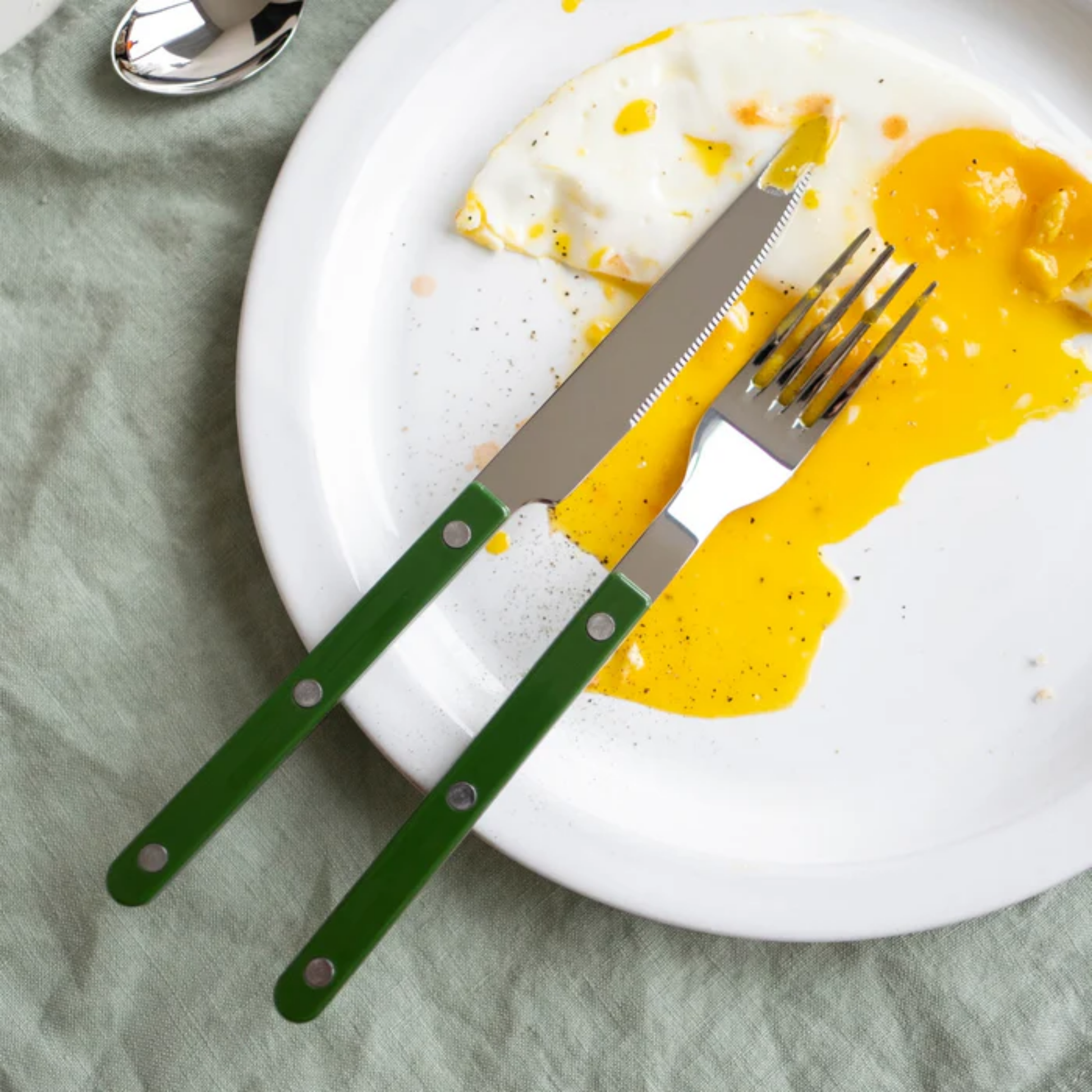On a plate with a fork and egg Sabre Paris Bistrot Dinner Knife Dark green - 24cm stainless steel knife with colorful nylon handle and visible rivets. Inspired by French café style, this elegant and durable knife combines traditional charm with modern flair, available in gloss or vintage finishes and dishwasher-safe.