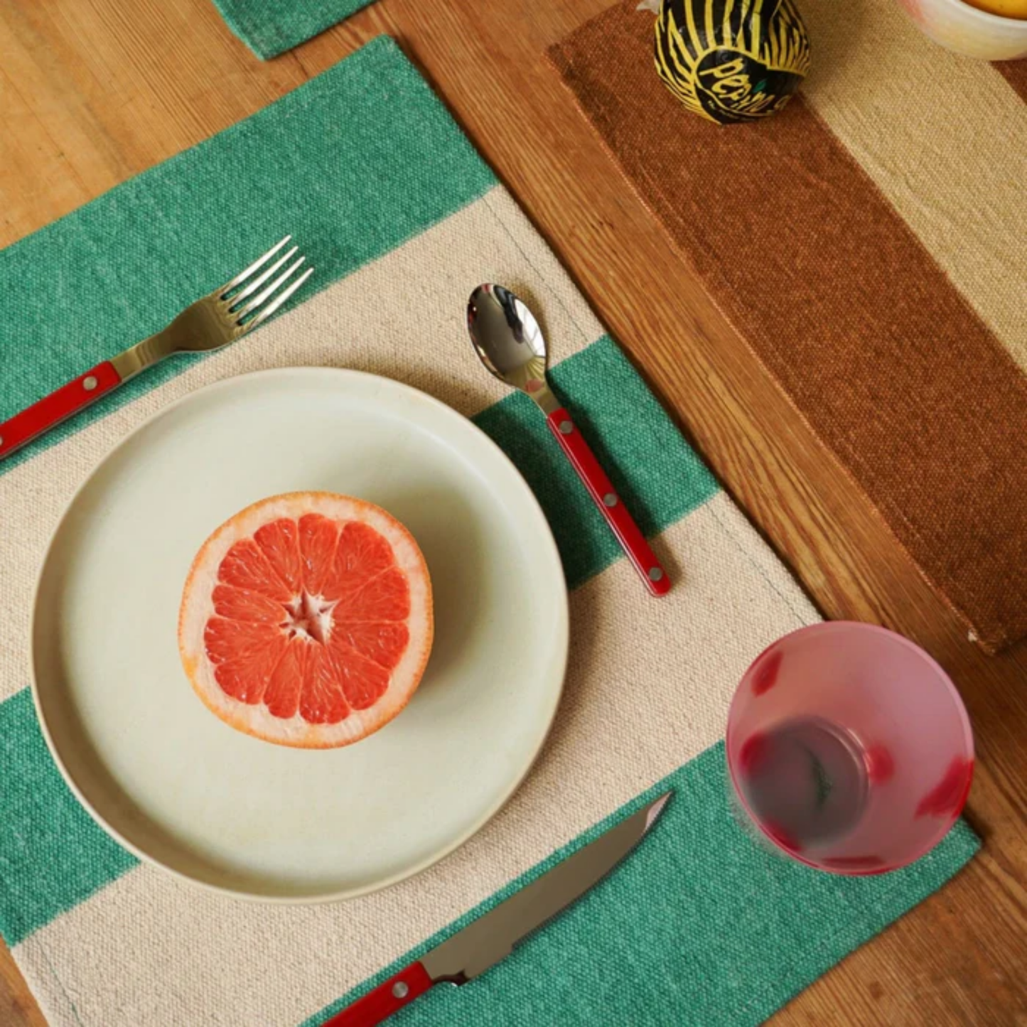 Fork and knife on a table mat with Sabre Paris Bistrot Soup Spoon Burgundy - 22cm stainless steel spoon with colorful nylon handle and visible rivets. Inspired by French cafés, this large, elegant, and durable soup spoon comes in gloss or vintage finishes and is dishwasher-safe.