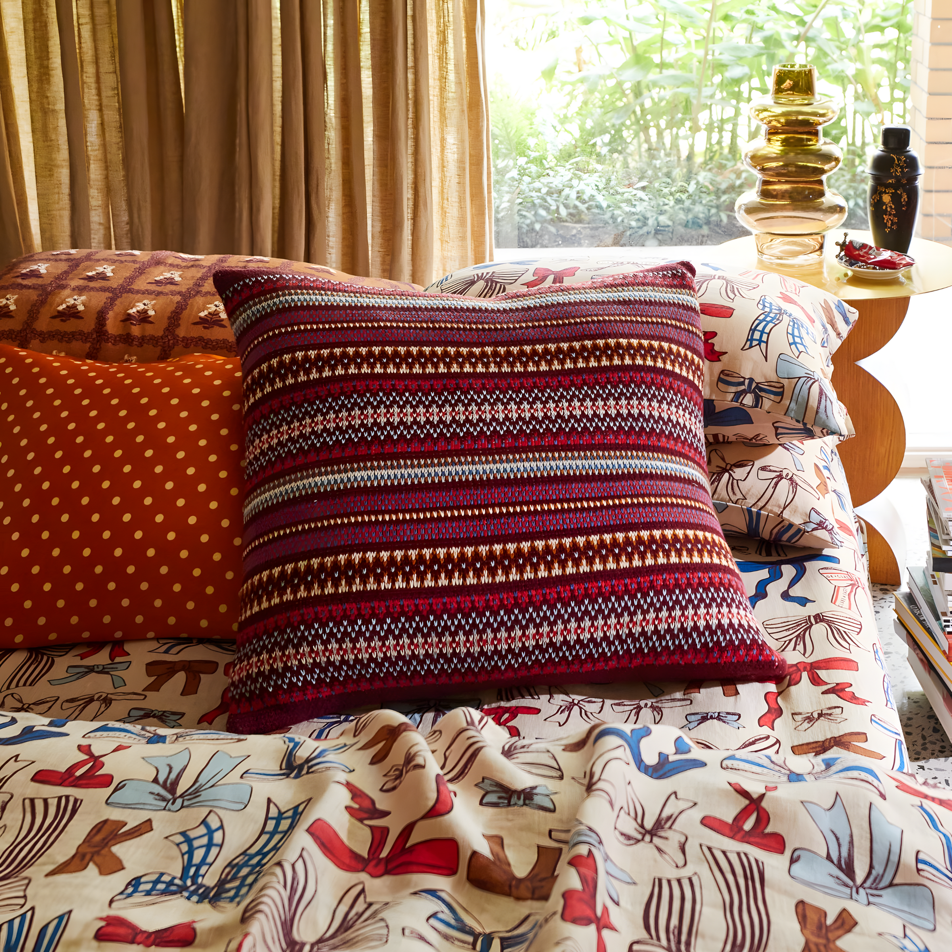 Shown on the bed with other smaller pillows at the back, Sage & Clare Arlette Knit Cushion in Mahogany, a 65×65cm cotton Fair Isle textured decorative throw pillow with premium soft insert.