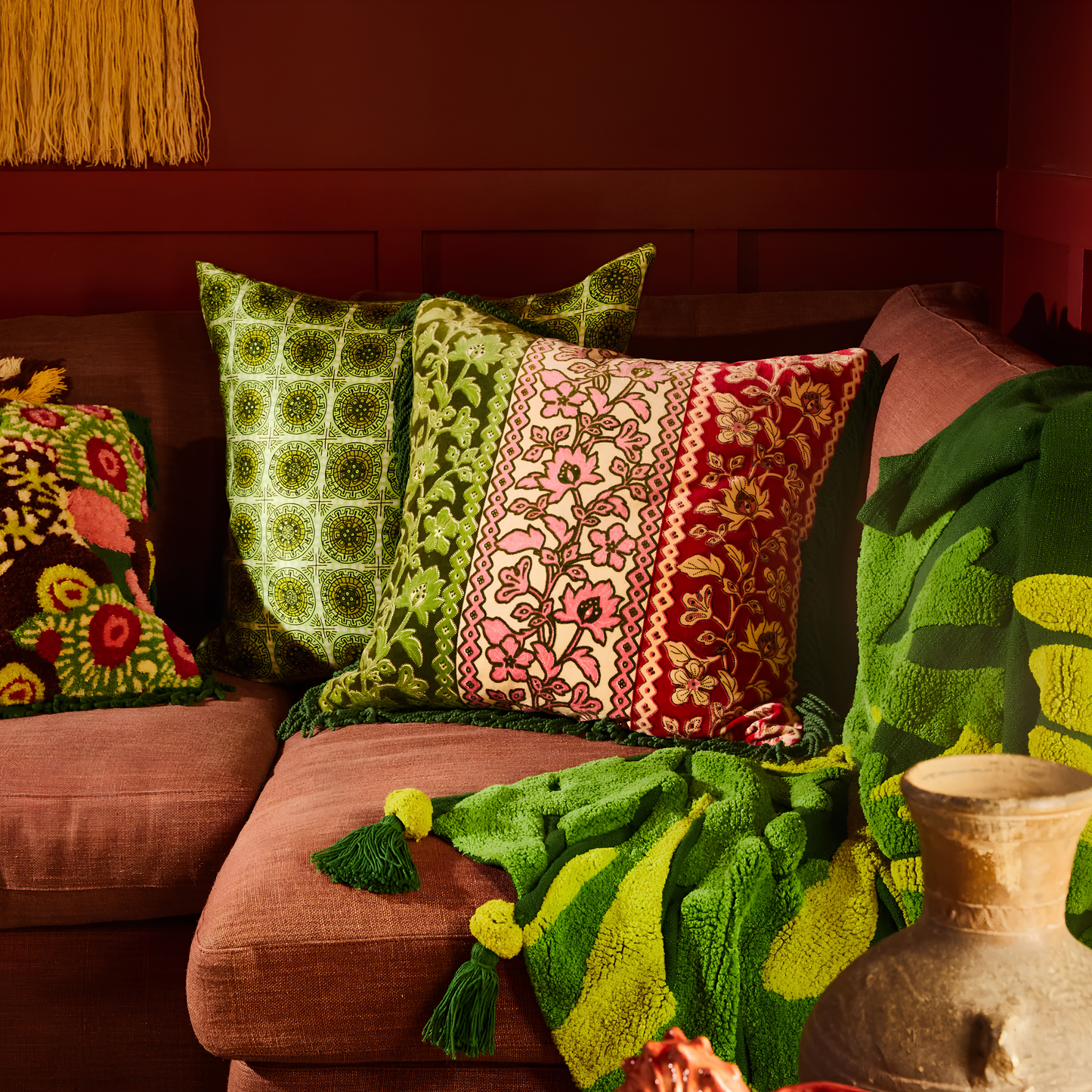 Leaning on the couch with other pillows, the Sage & Clare Cushion Thea Velvet Kelp with plush texture, floral design, fringe edges and high quality insert.