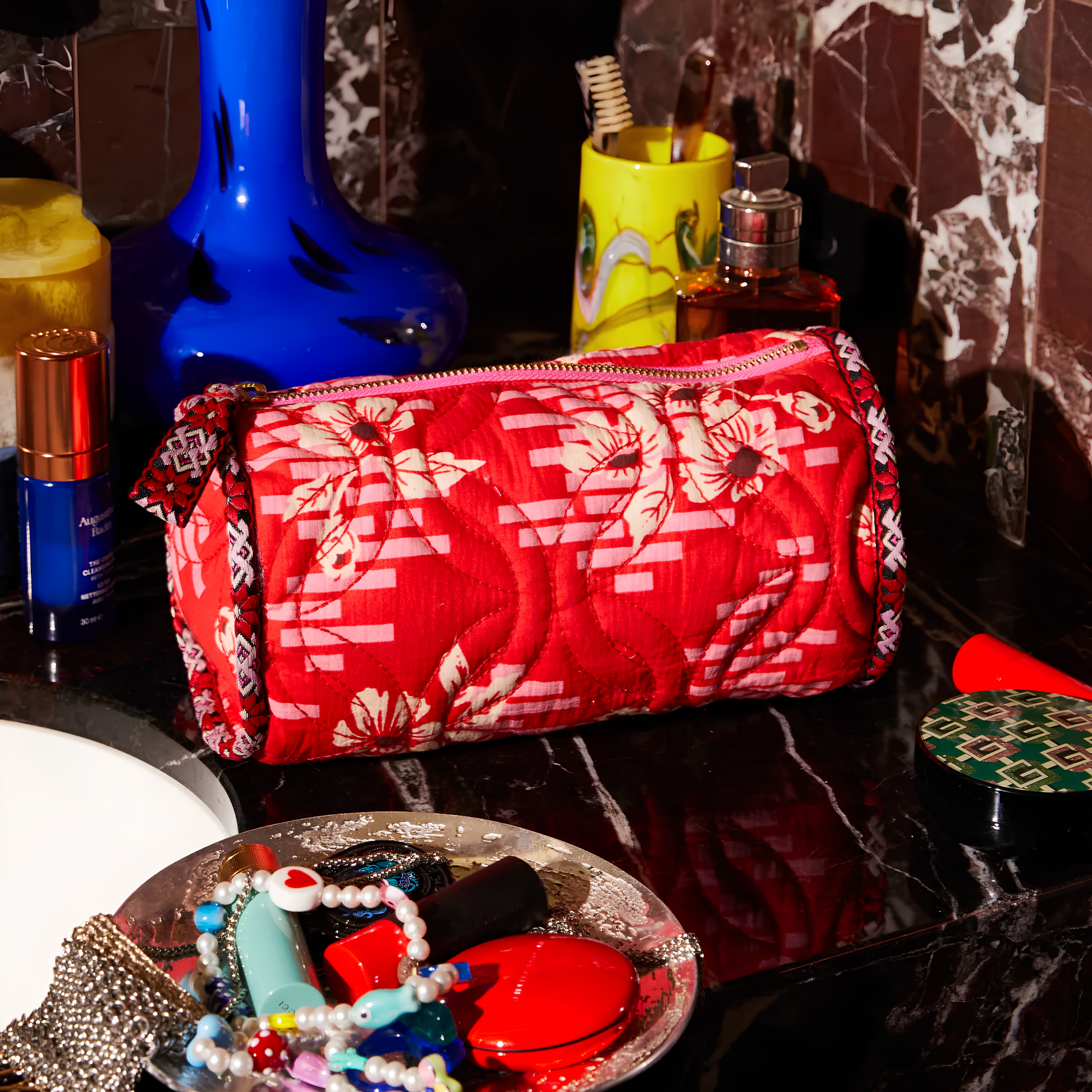 Sage & Clare Makeup Bag Marta Vermillion round and roomy with wide zip opening, lightly quilted and a compact design, seen on the vanity countertop.