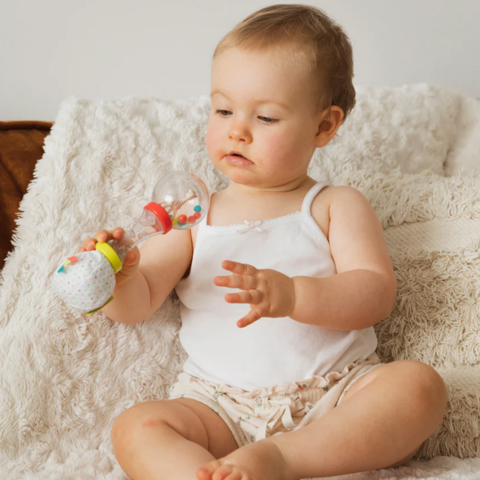 Baby playing with rattle from maracas set on fluffy blanket