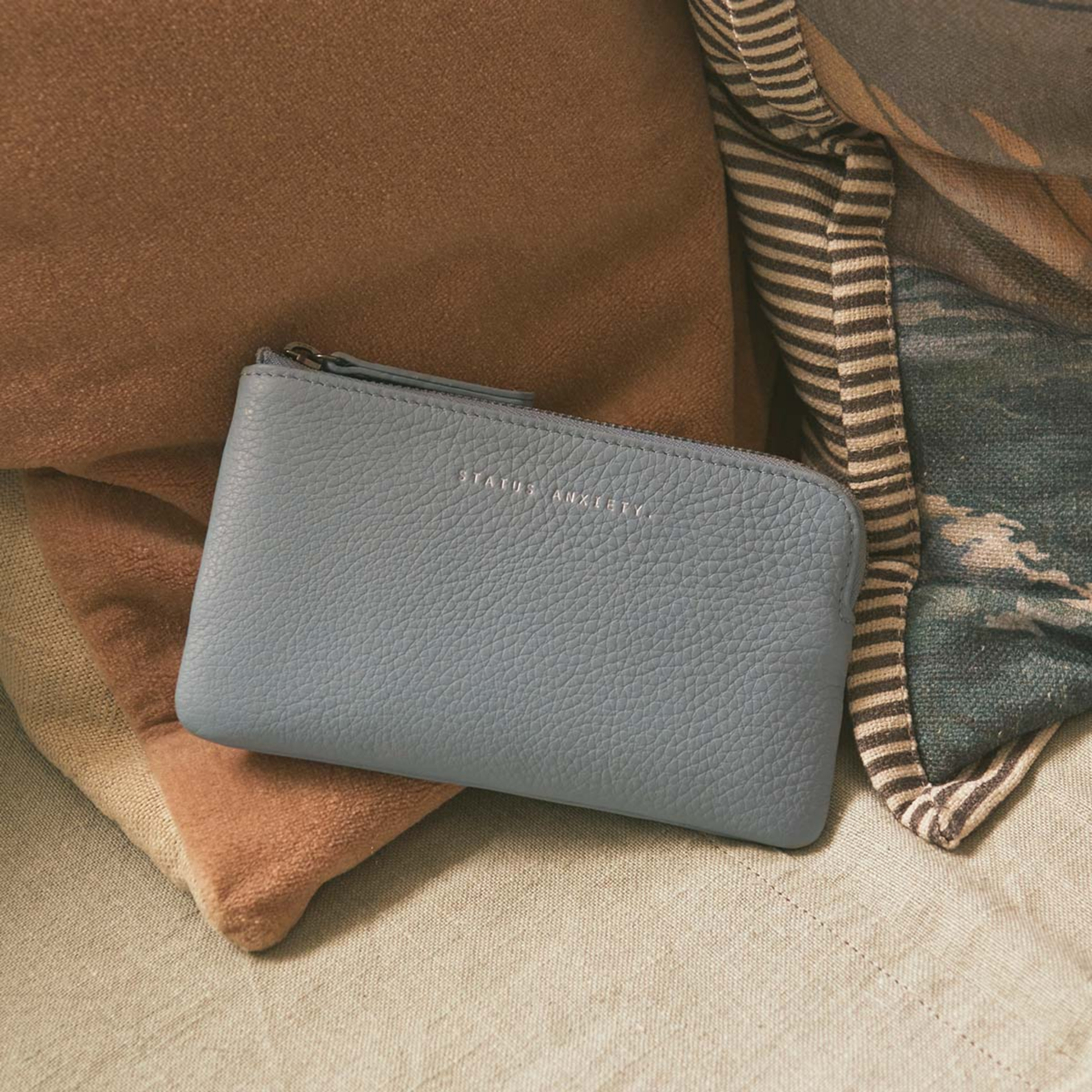 Front view with pillows, the Status Anxiety Wallet Smoke And Mirrors Powder Blue from soft shrunken pebble leather with 4 card slots.