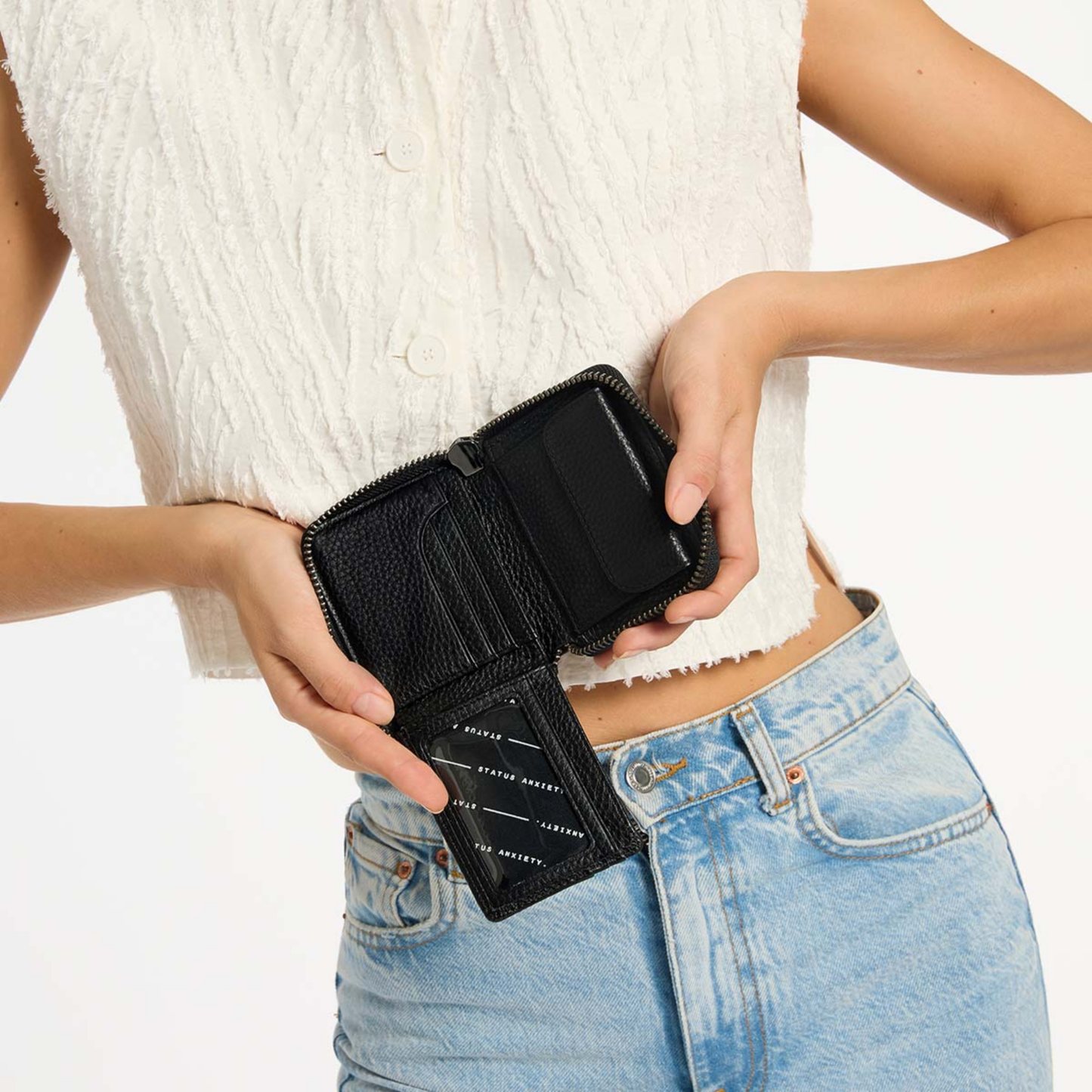 Open Status Anxiety Wallet Wayward Black from shrunken pebble leather with zipper, silver foil logo and 9 slots, held.