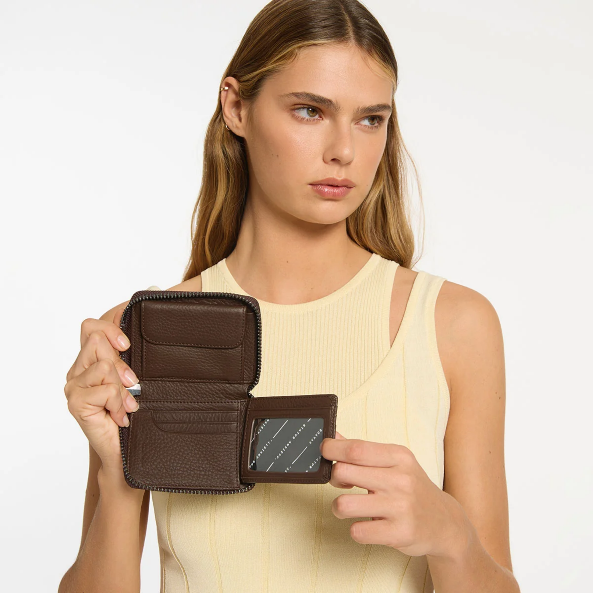 Open Status Anxiety Wallet Wayward Cocoa from shrunken pebble leather with zipper, silver foil logo and 9 slots, held by a woman.