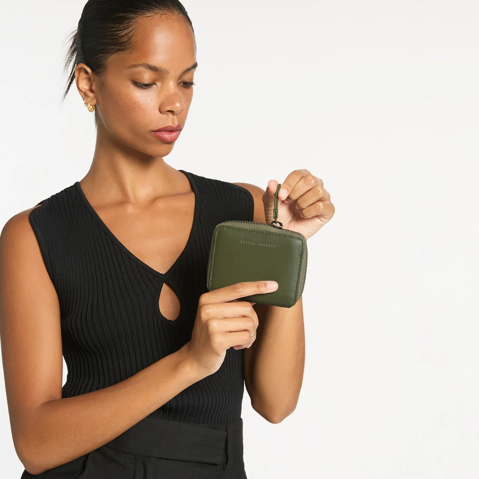 Front view of the Status Anxiety Wallet Wayward Khaki from shrunken pebble leather with zipper, silver foil logo and 9 slots, held by a woman.