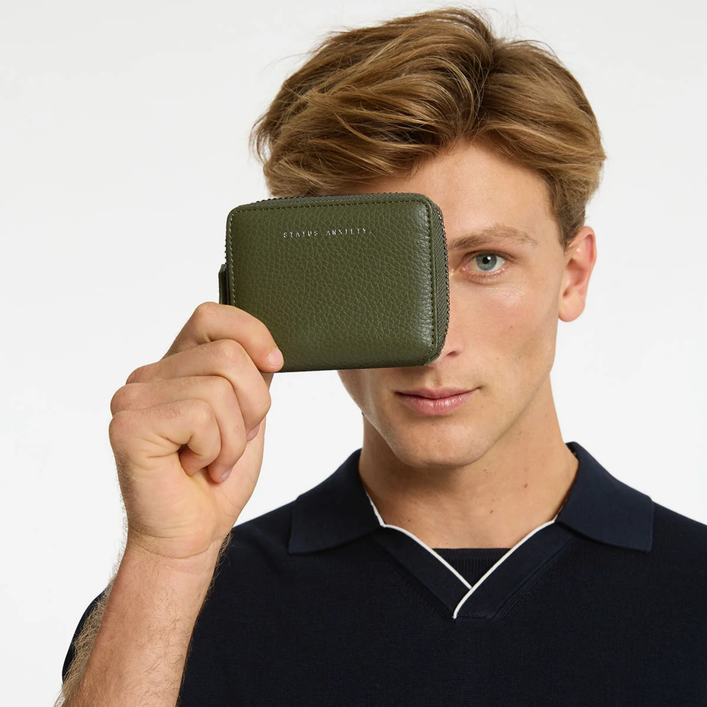Status Anxiety Wallet Wayward Khaki from shrunken pebble leather with zipper, silver foil logo and 9 slots, held face level.