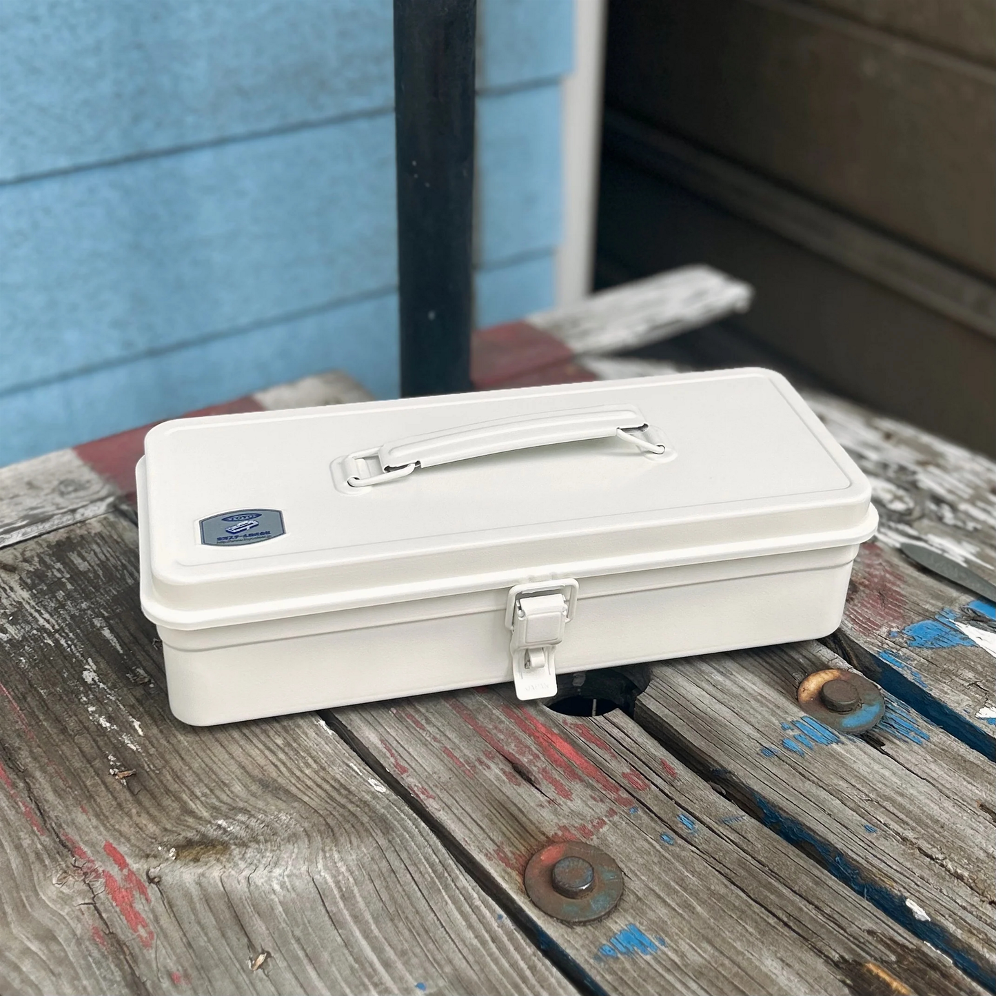 Outside on a wooden surface, the Closed Toyo Toolbox Trunk Shape T-320 White crafted from a single pressed steel, smooth and rounded design with matte texture that's gentle on hands.