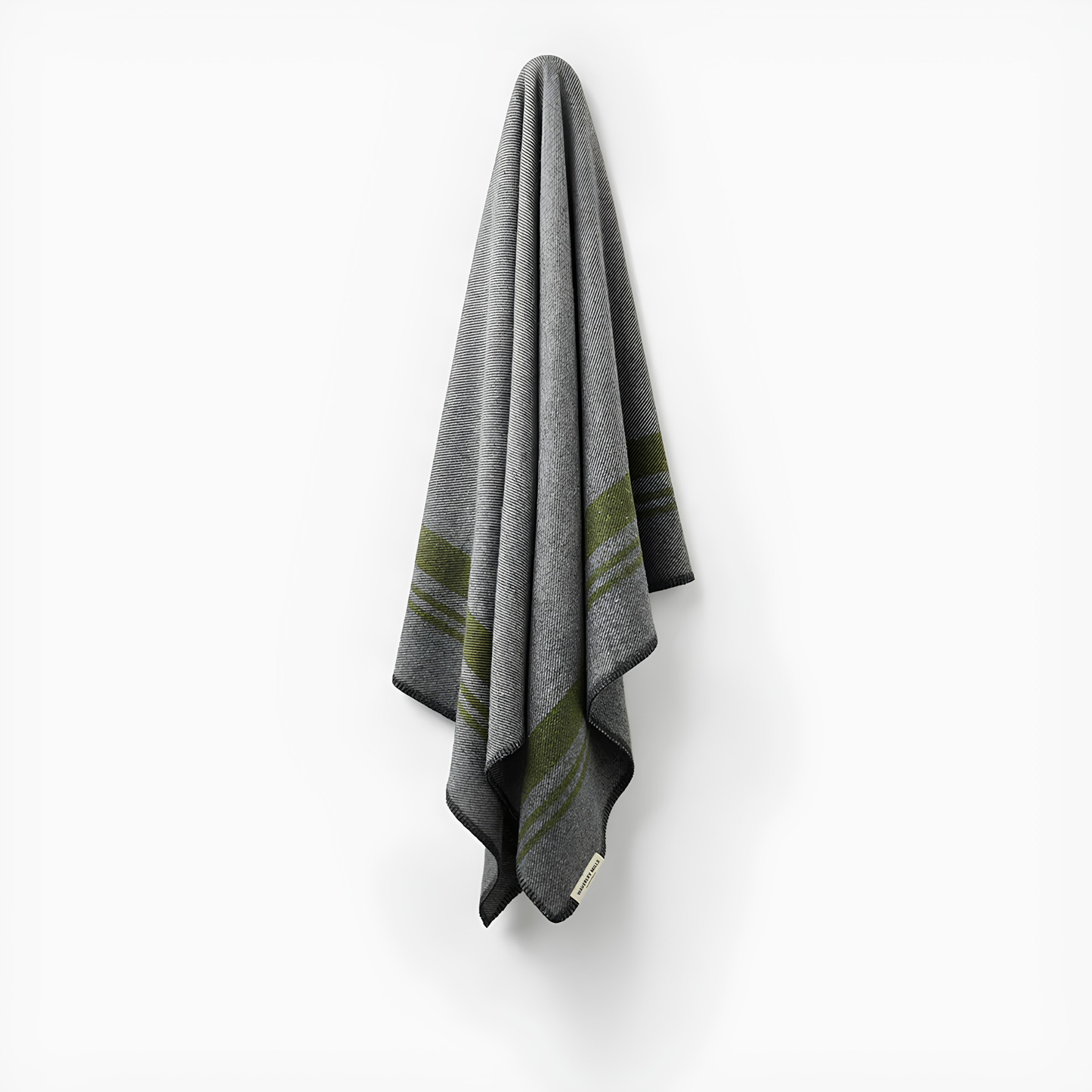 Hung on the wall, the Waverley Mills Field Blanket Charcoal from military origins, charcoal whip stitch fringe, and recycled wool in charcoal and grey with green stripe.