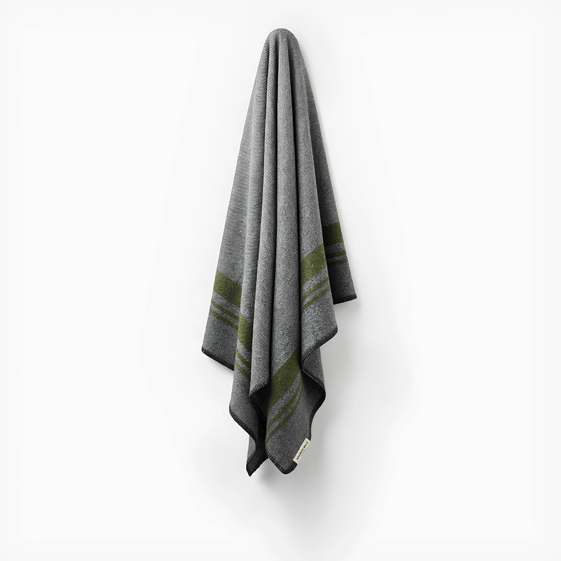 Hung on the wall, the Waverley Mills Field Blanket Charcoal from military origins, charcoal whip stitch fringe, and recycled wool in charcoal and grey with green stripe.