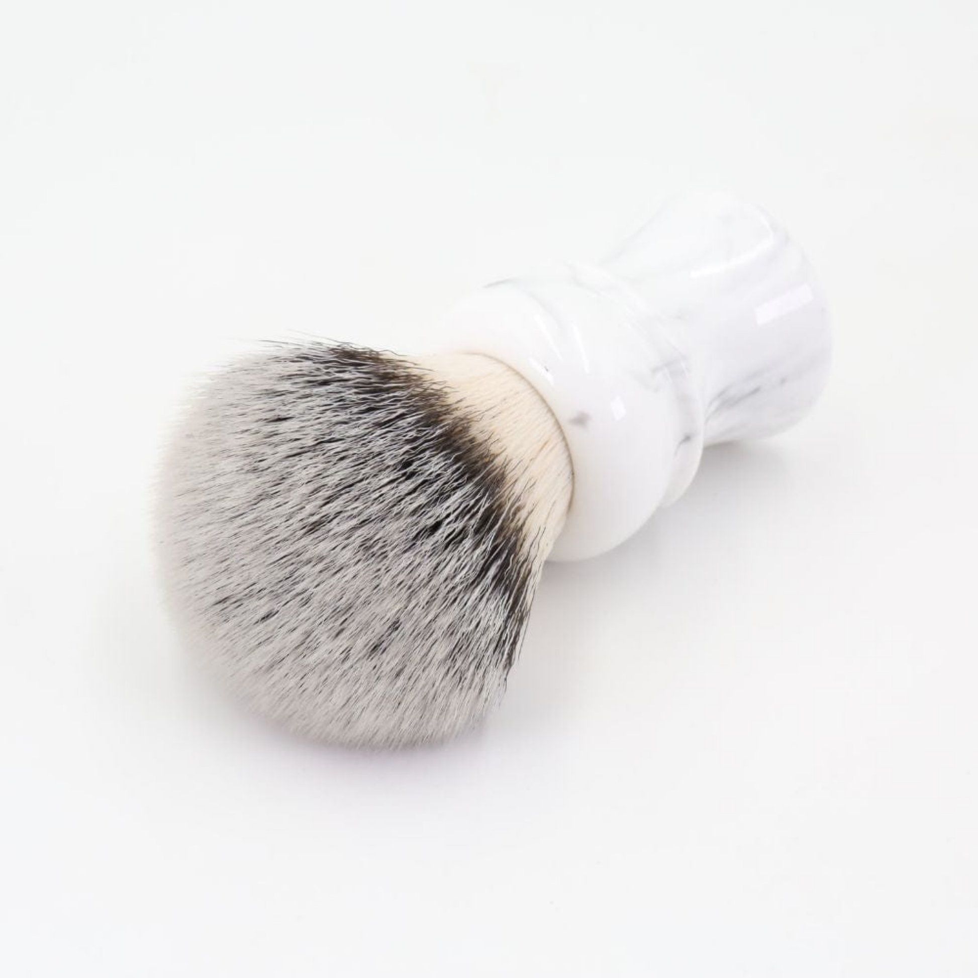 Yaqi White Marble Synthetic Shaving Brush, laid down on a surface- 24mm nylon bristles, 52mm loft, marble resin handle, quick-drying, dense brush for smooth wet shaving.